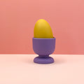 Yellow egg in a purple egg cup on a pink background