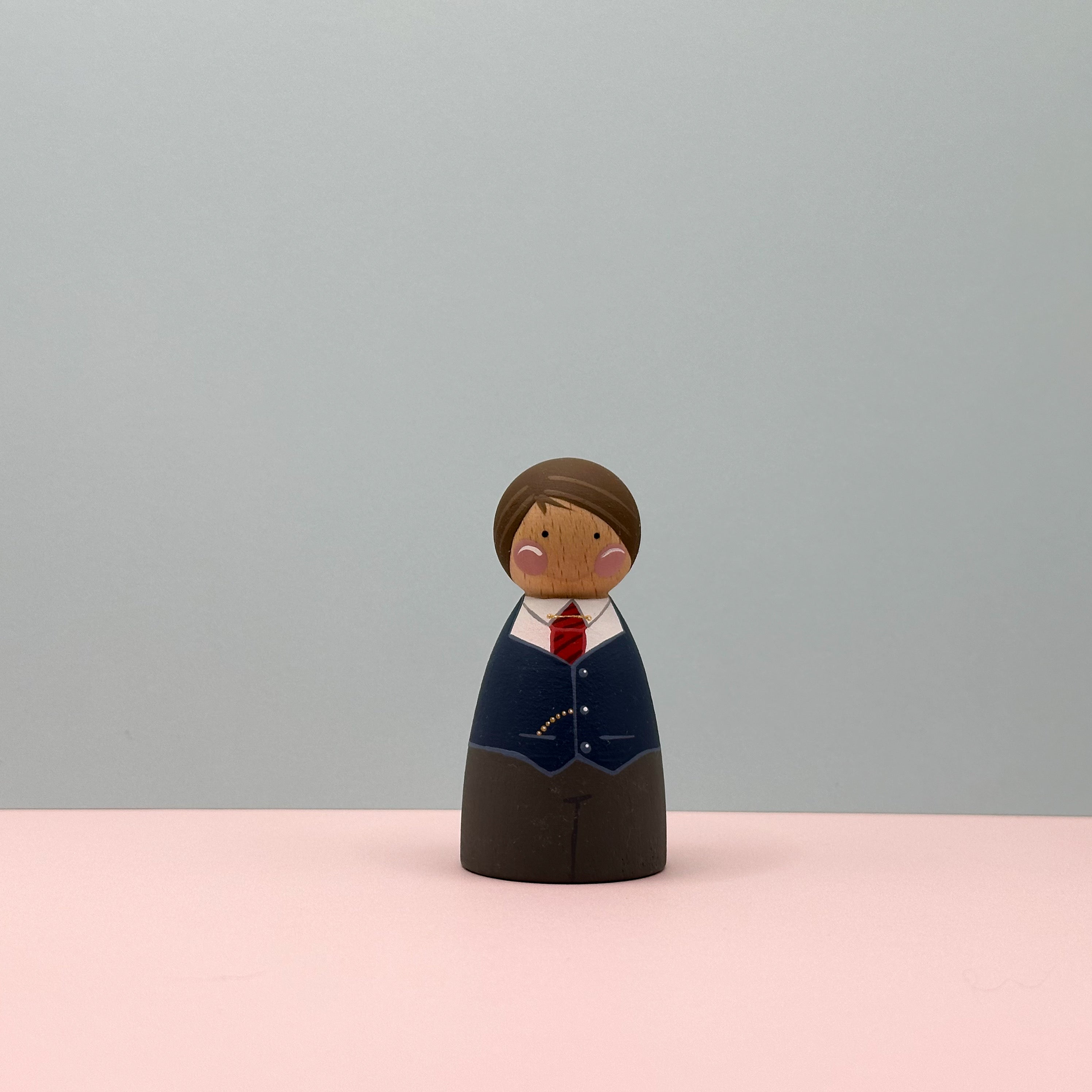 Wooden figurine of a person wearing a suit and tie on a pink and gray background