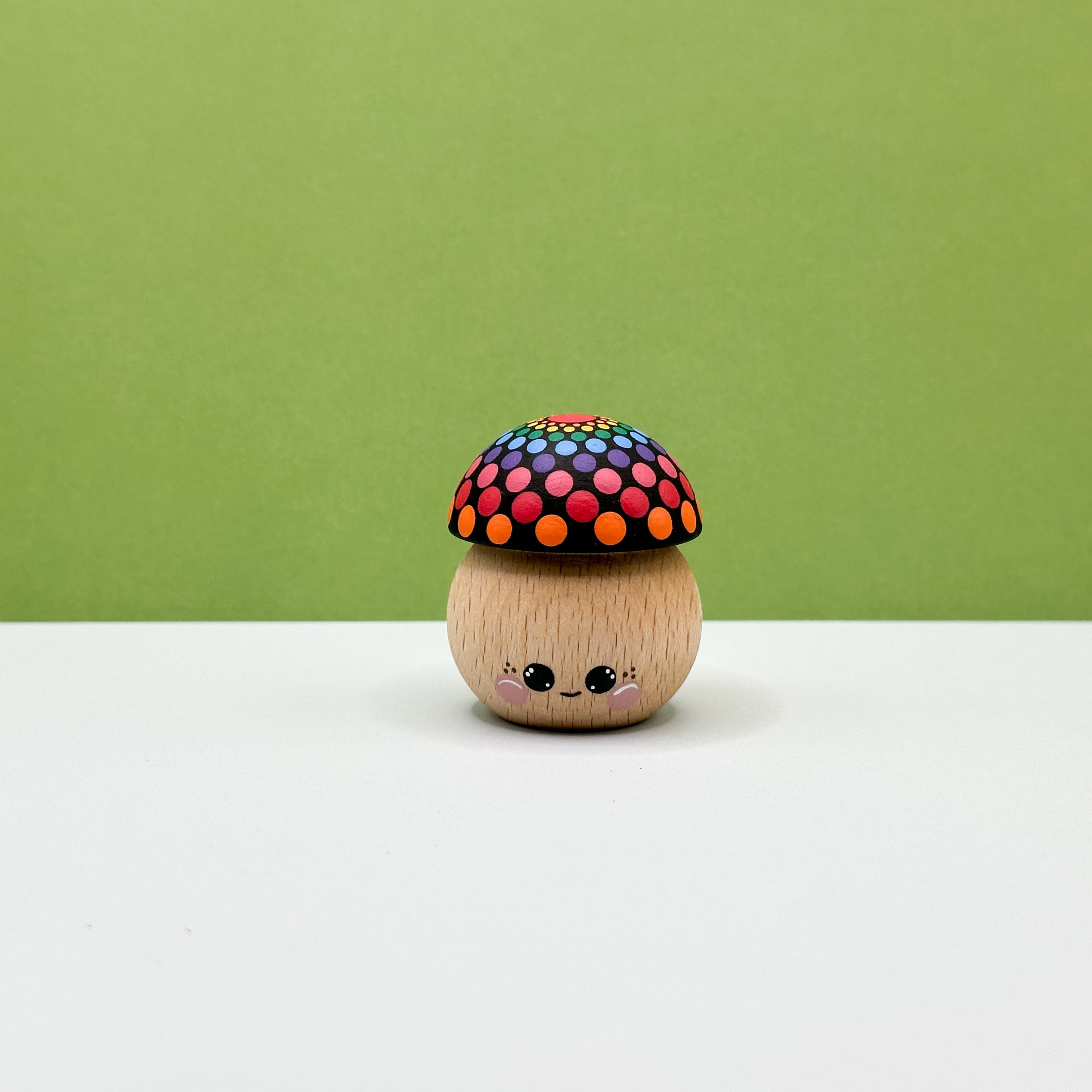 Wooden toy mushroom with a colorful polka dot cap on a white surface with a green background