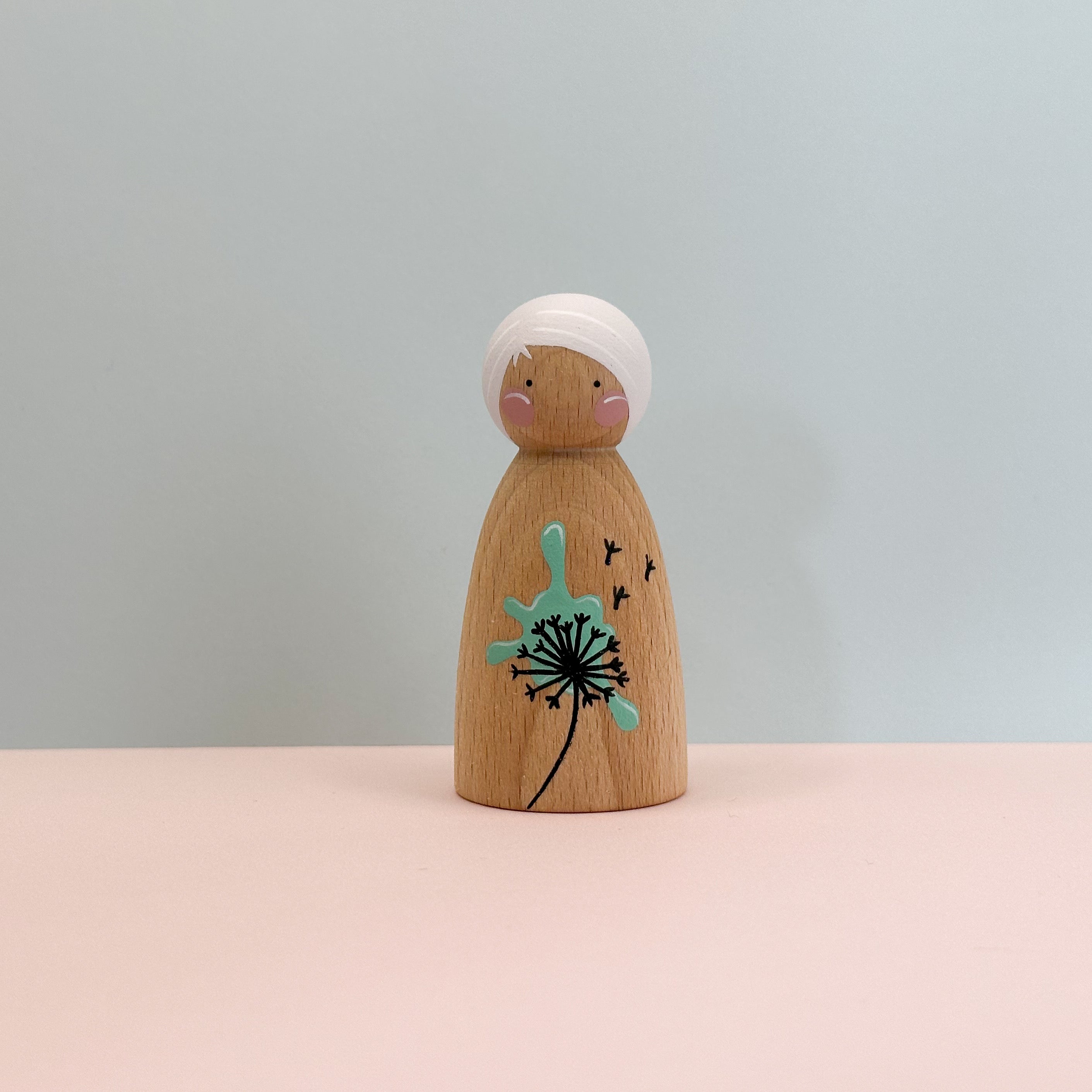 Wooden peg doll with a dandelion design on a light gray background