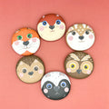 Set of six animal-themed wooden pebbles on a pink background