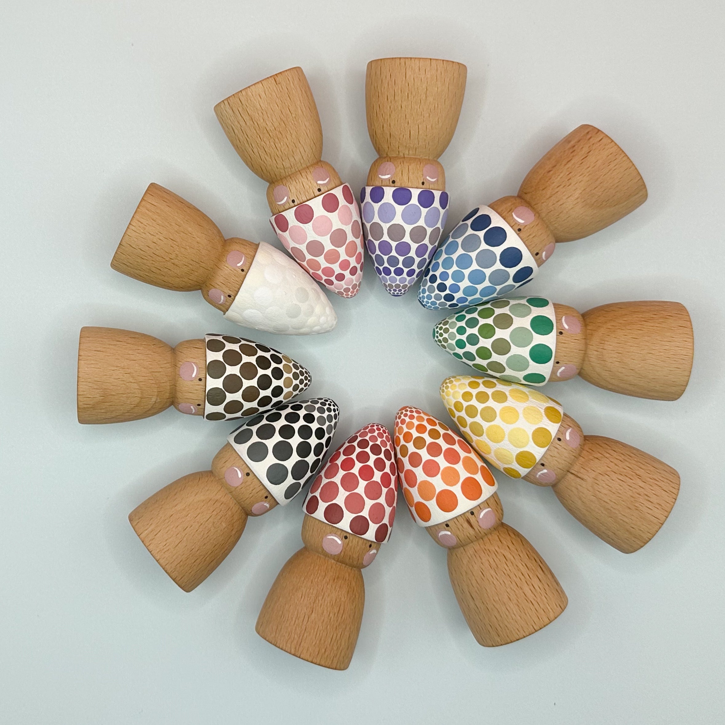 Wooden pegs with colorful polka dot patterns arranged in a circular pattern on a light gray background.
