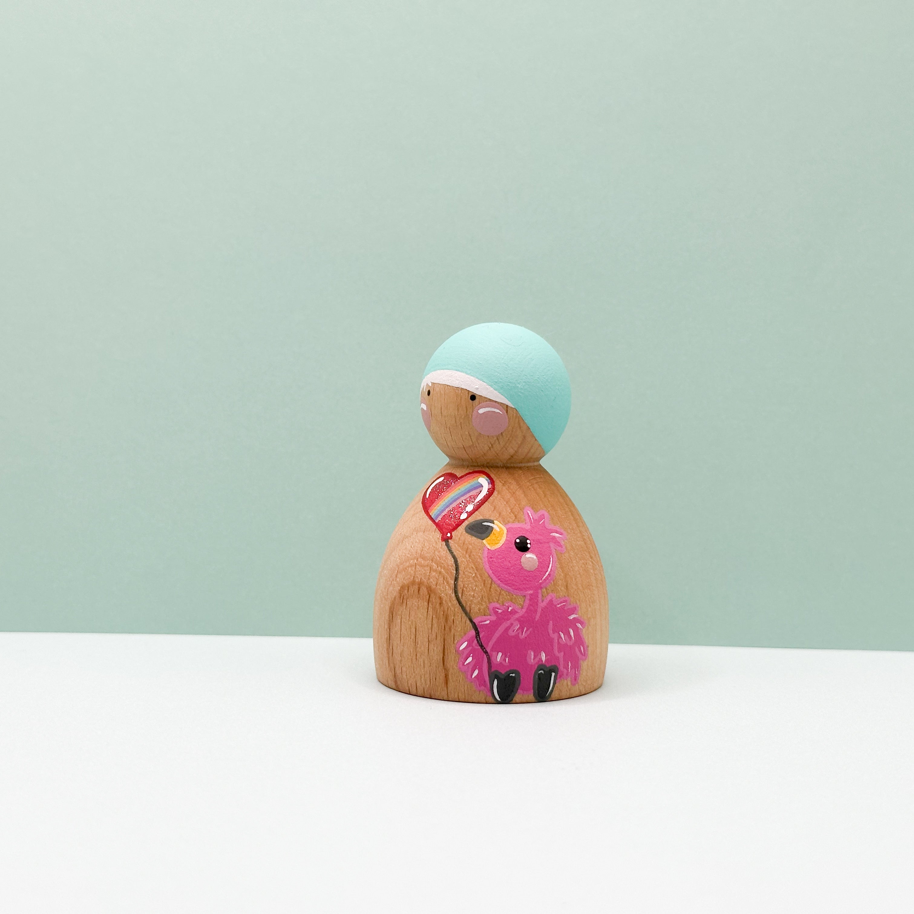 Wooden peg doll with a pink flamingo design on a light green background
