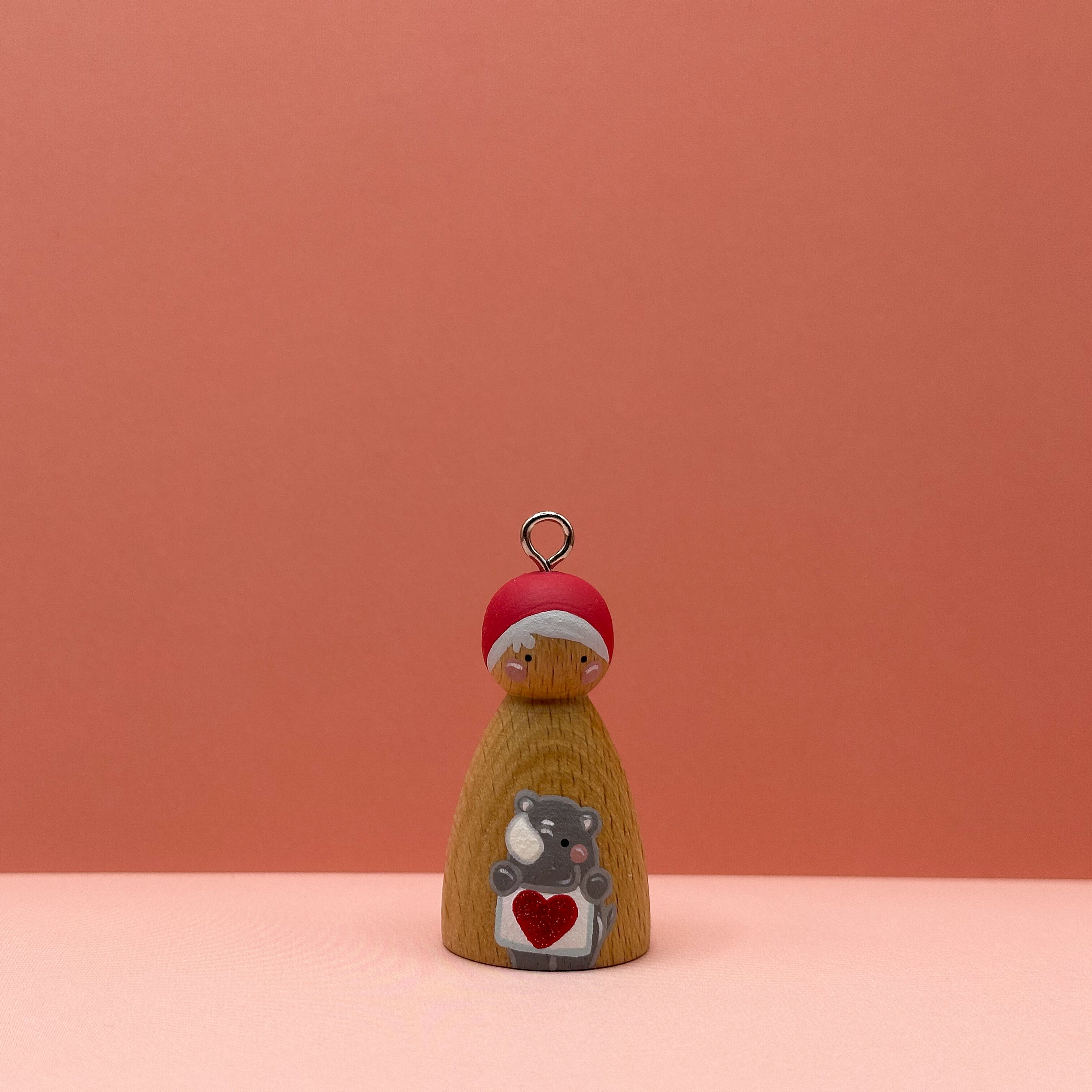 Small peg doll keyring with a rhino holding a heart sign painted on its body with a peach background