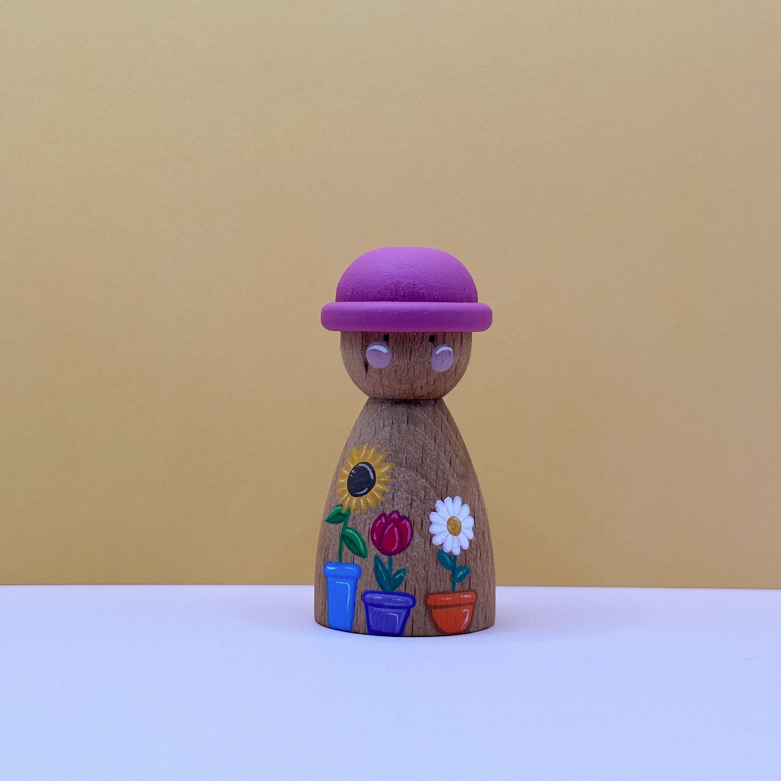 Wooden peg doll with a pink  hat and painted flowers on a beige background