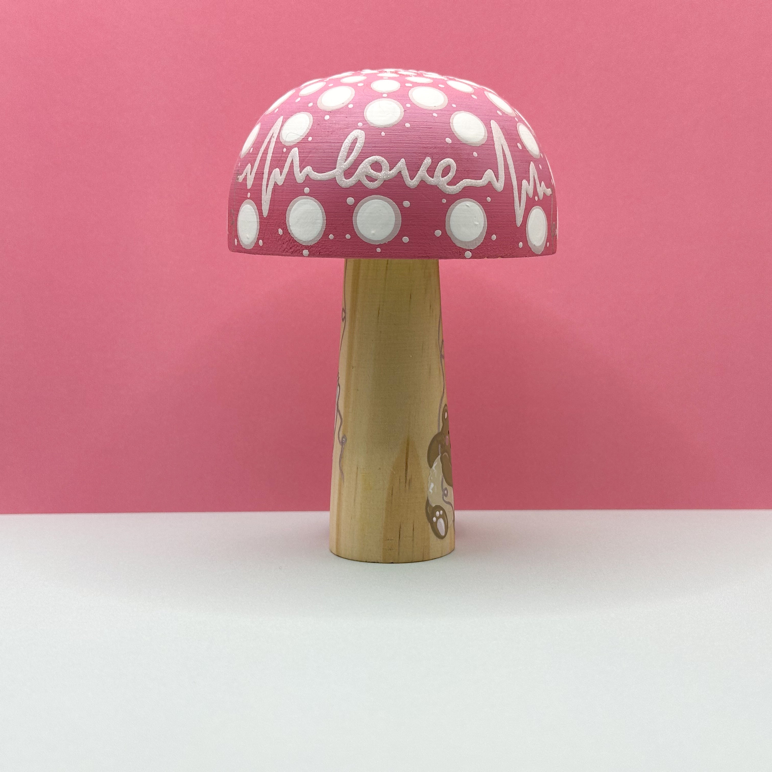 Mushroom-shaped toy with pink polka dot shade and wooden base on a pink background