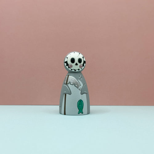 Small figurine with a skull-like head and green fish on a pink background