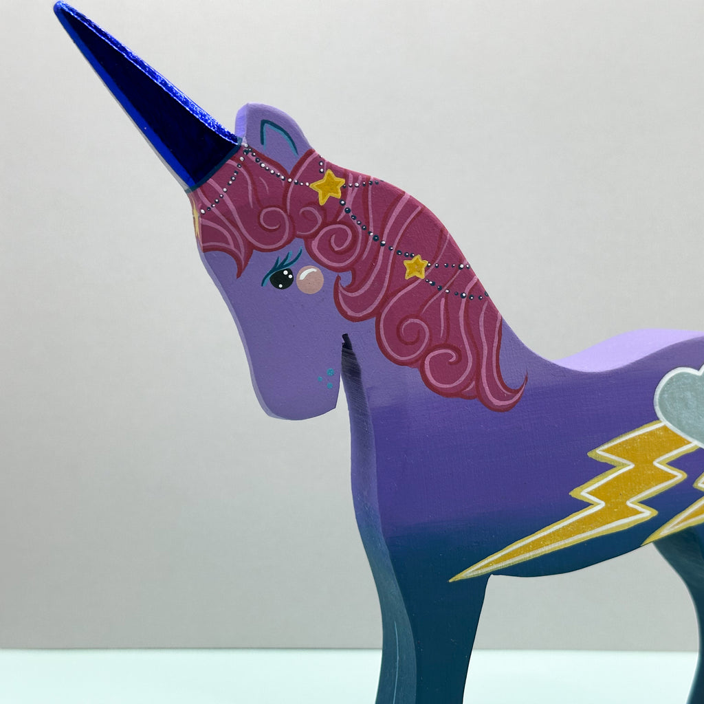 Colorful unicorn figurine with purple body and blue horn on a light gray background