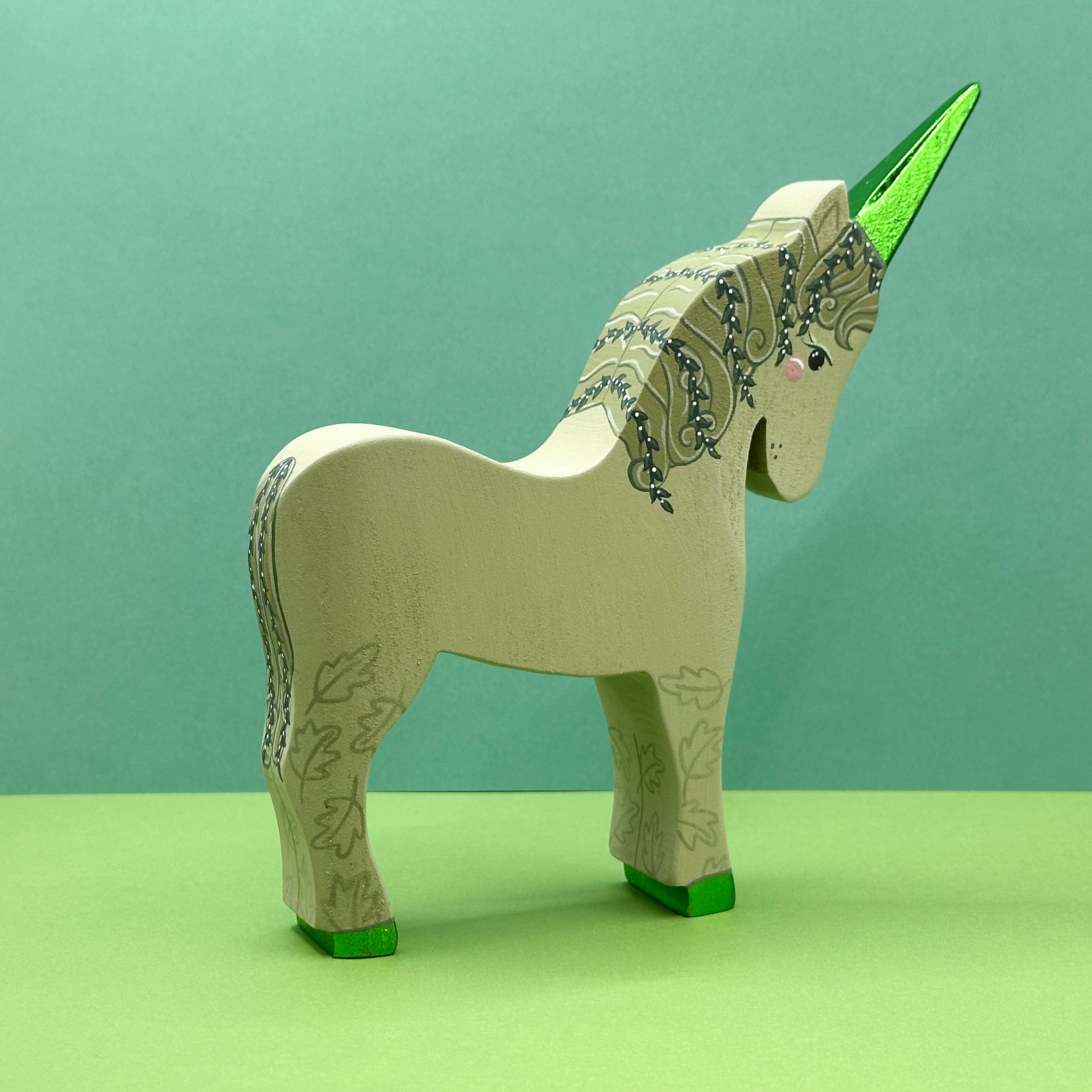 Wooden unicorn figurine with green horn and hooves on a green background