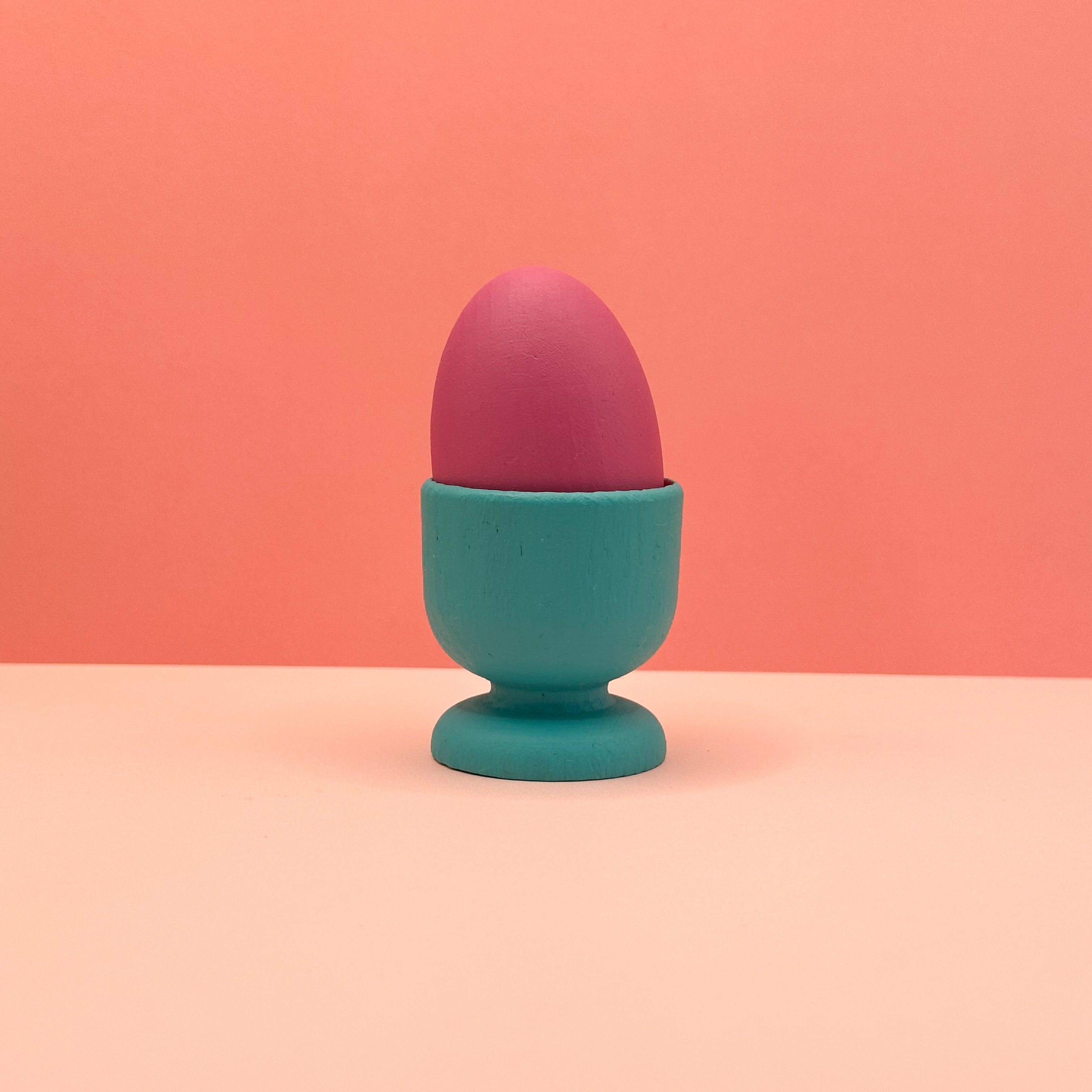 Pink egg in a blue holder on a peach background