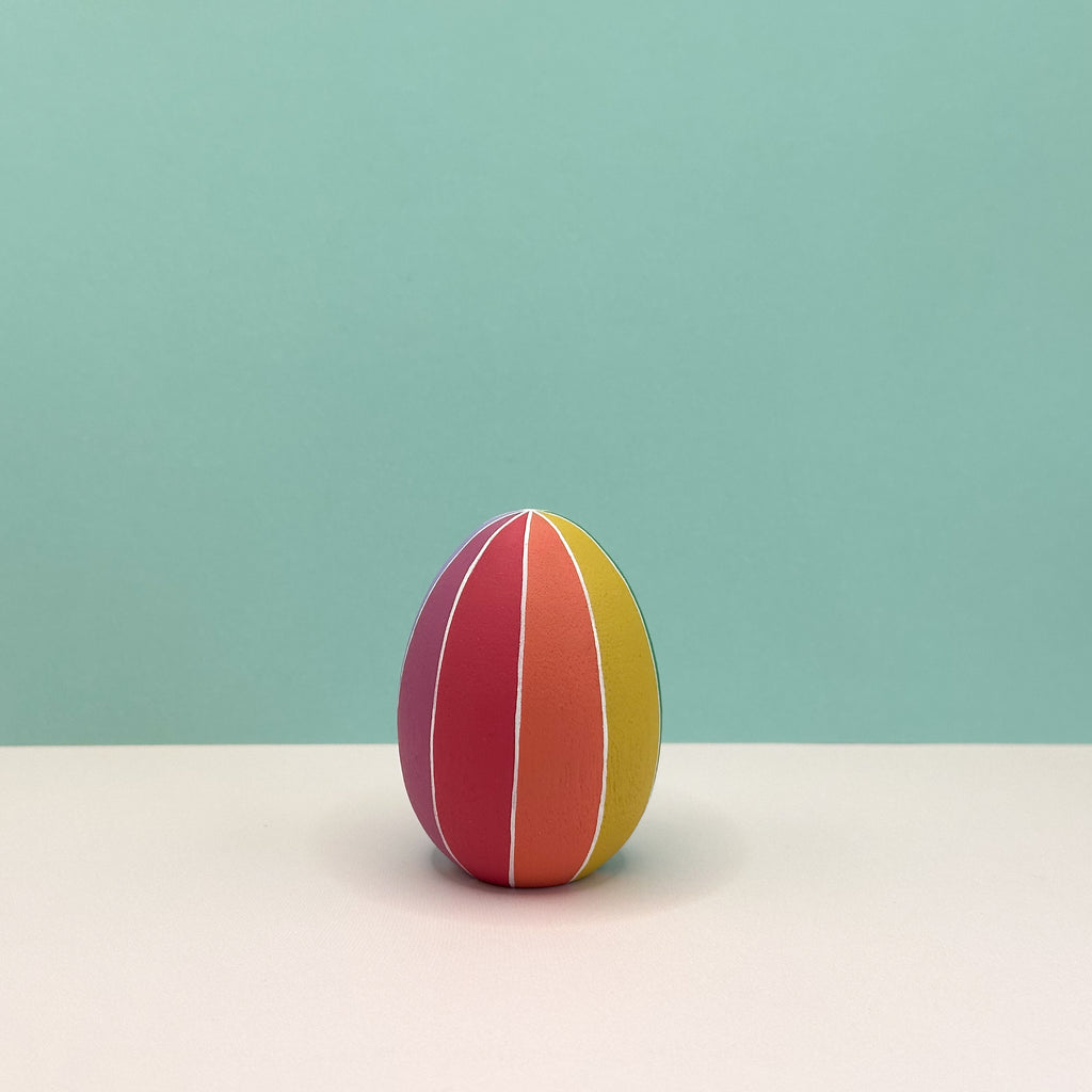 Colorful striped egg on a light beige surface with a light blue background