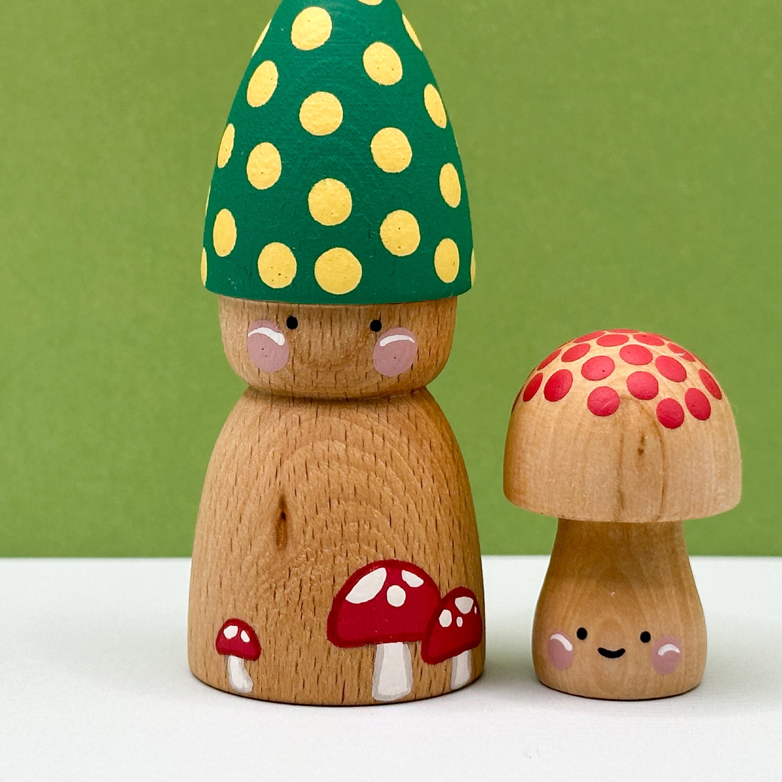 Two wooden mushroom figurines with colorful caps on a white surface against a green background