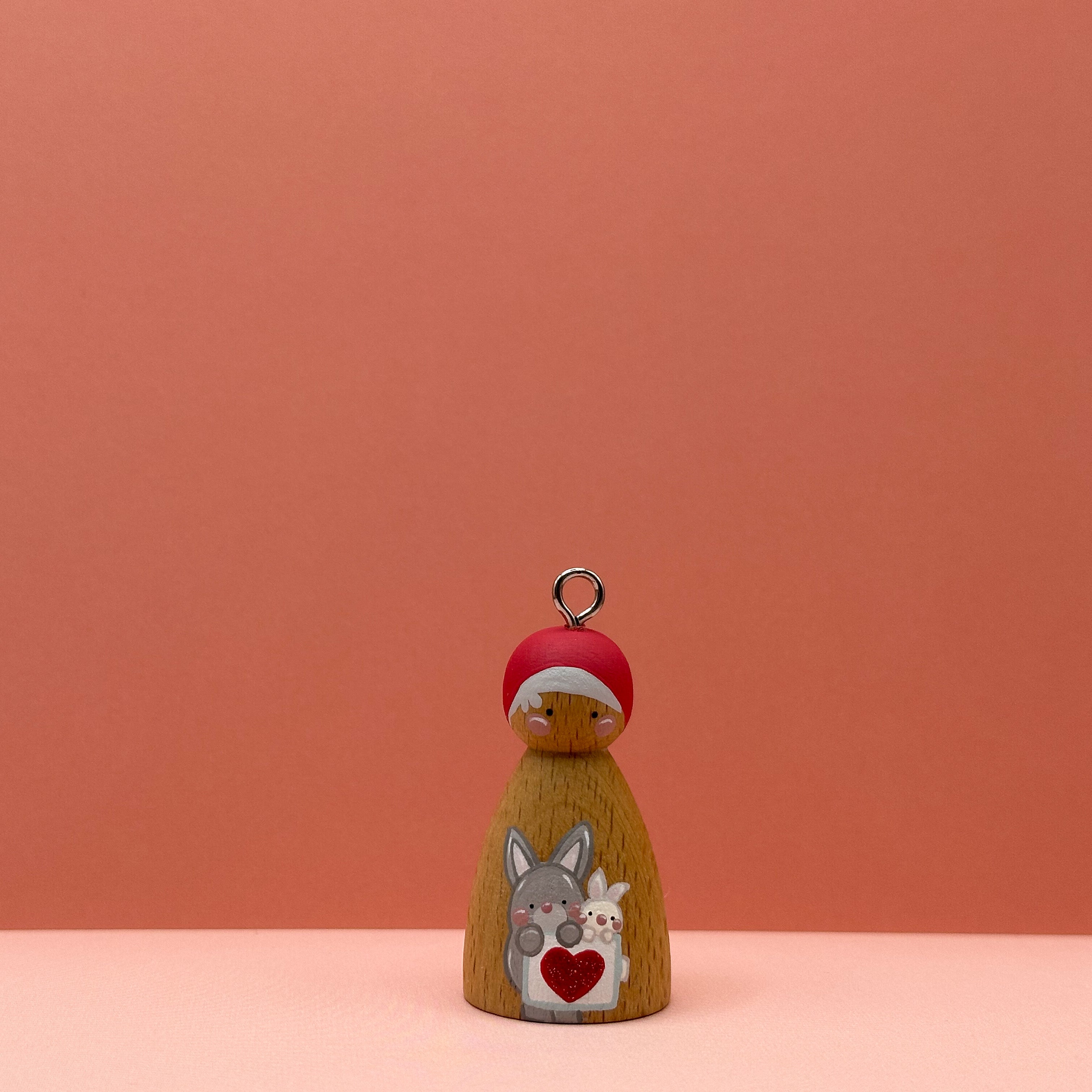 Small peg doll keyring with two rabbits holding a heart sign painted on its body with a peach background