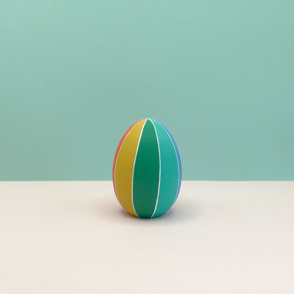 Colorful striped egg on a light beige surface with a light blue background