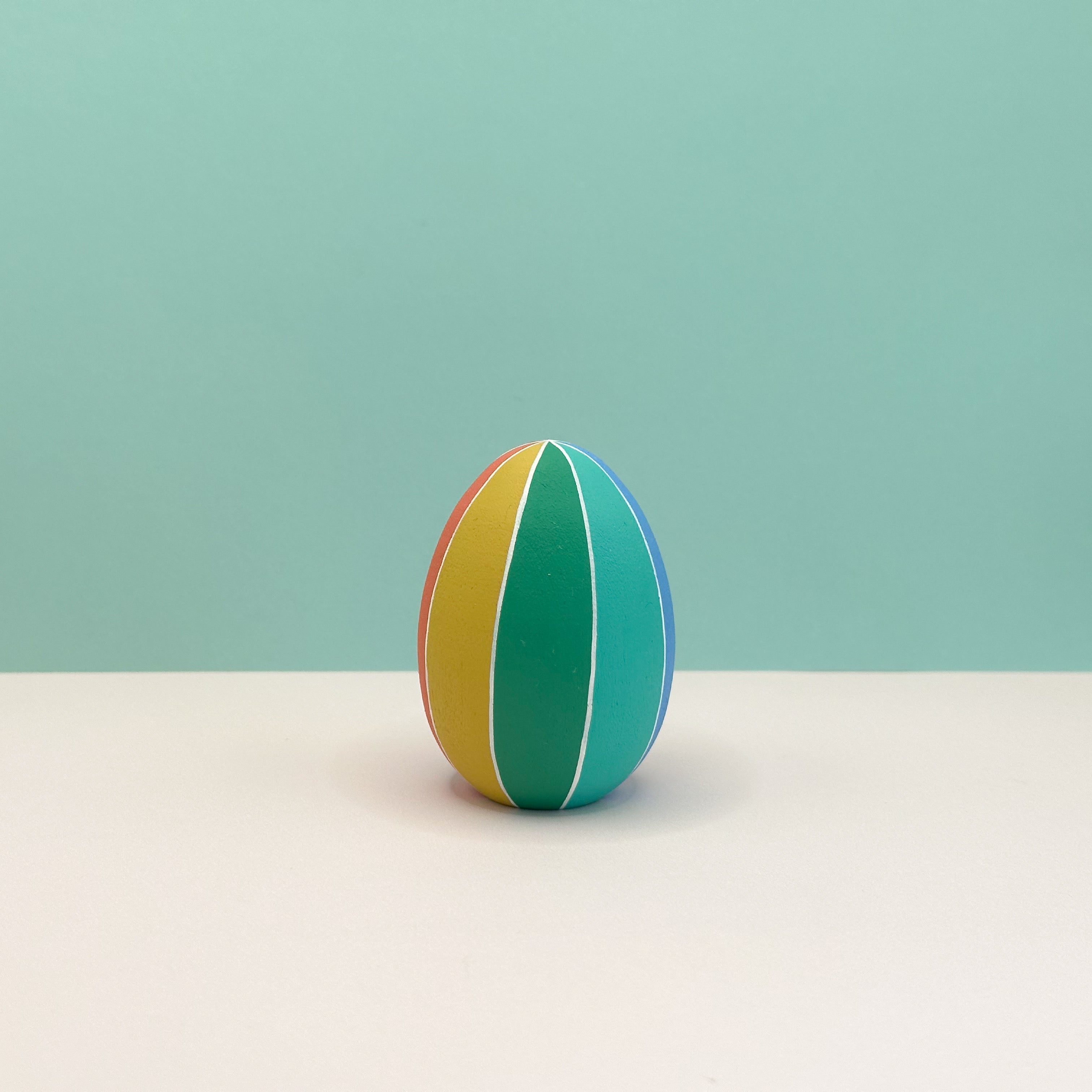 Colorful striped egg on a light beige surface with a light blue background