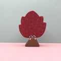 Decorative tree-shaped object with a face on a pink surface and light gray background