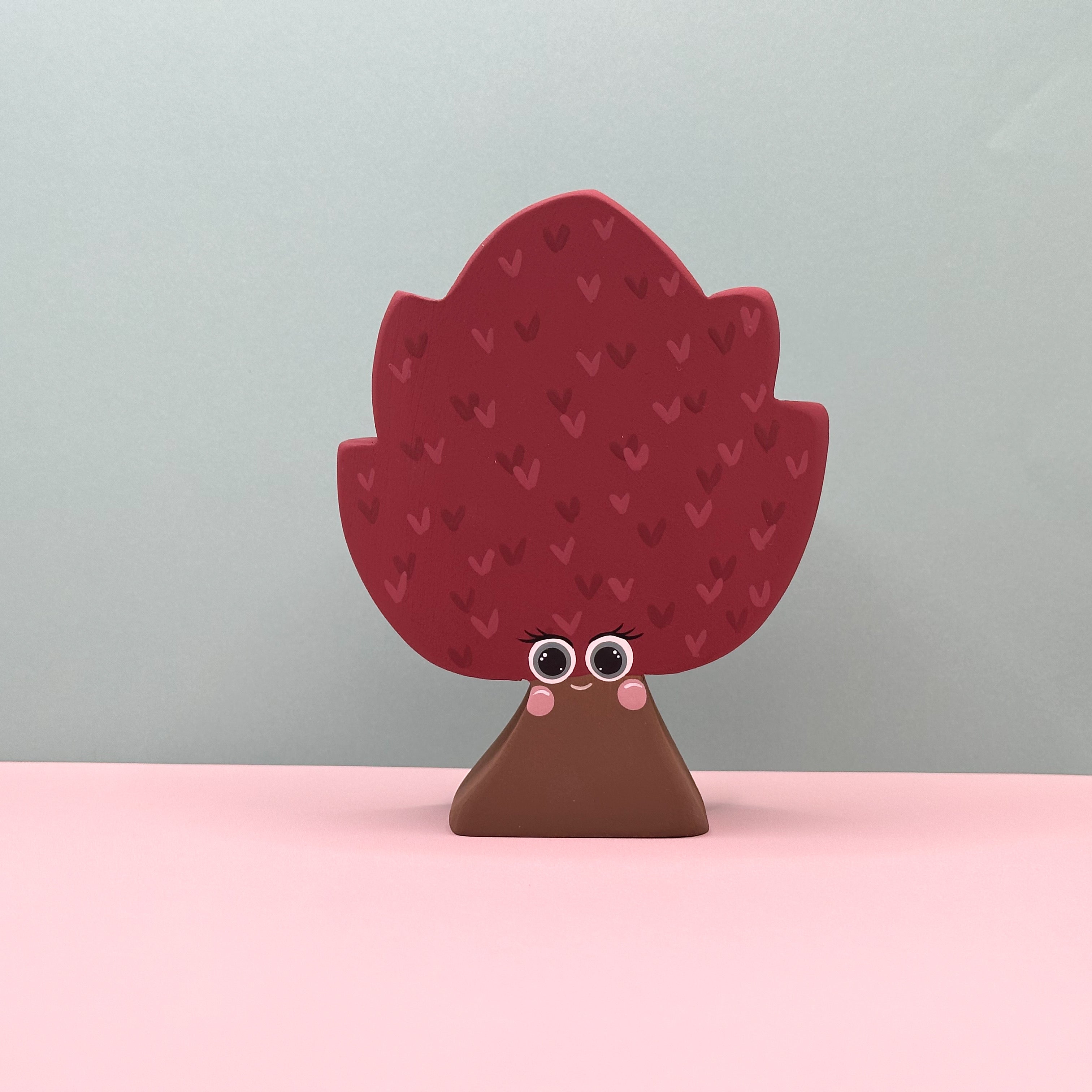 Decorative tree-shaped object with a face on a pink surface and light gray background
