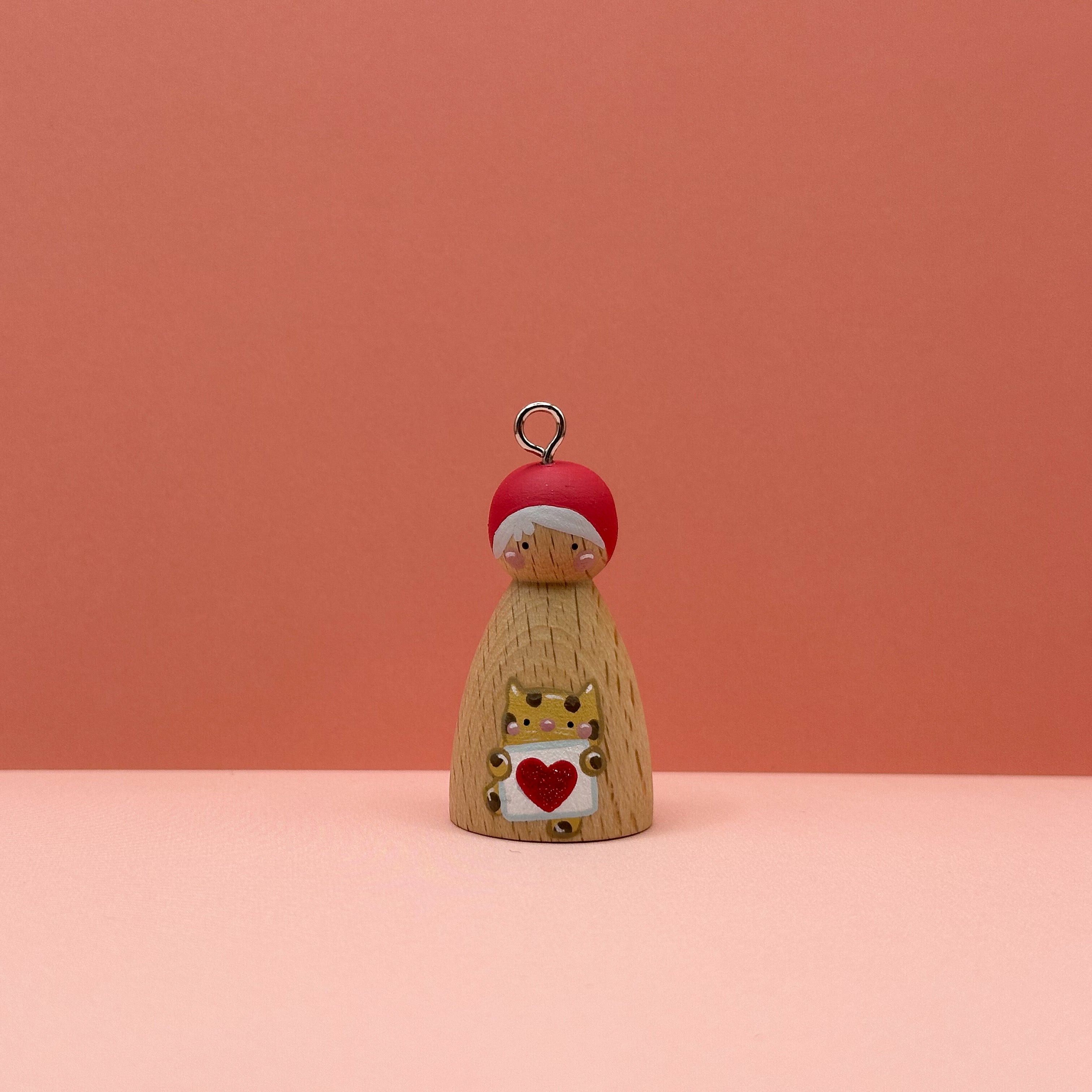 Small peg doll keyring with a cheetah holding a heart sign painted on its body with a peach background