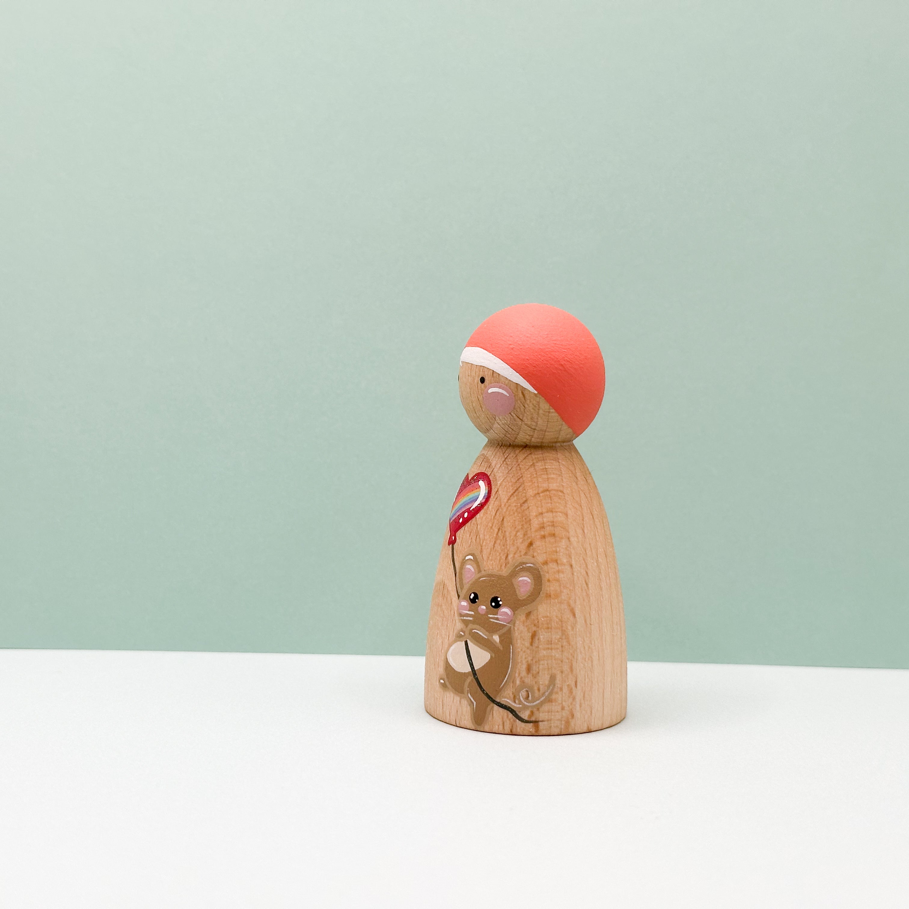Wooden peg doll with a red hat and a small mouse design on a light green background