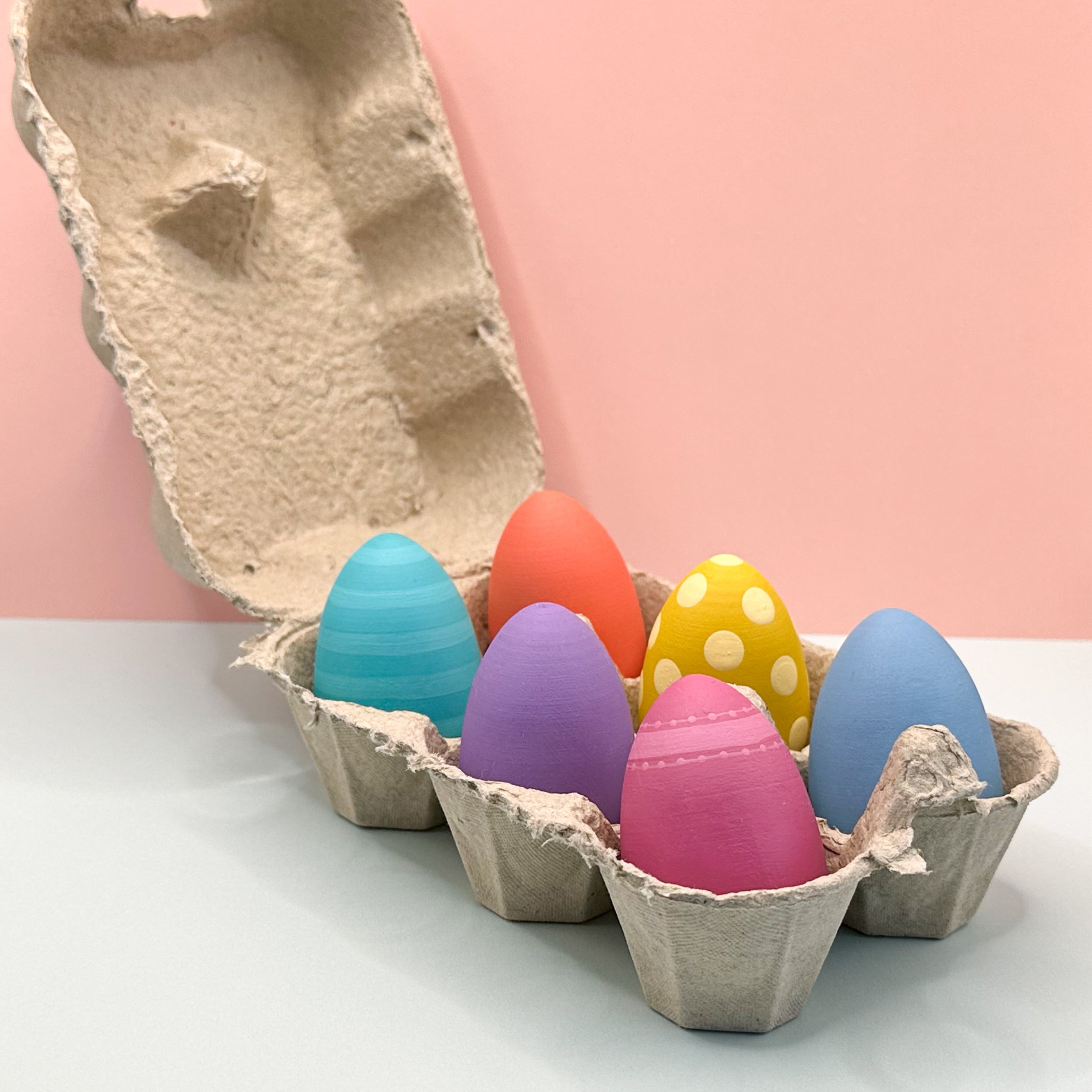 Colorful Easter eggs in a cardboard holder on a light pink background
