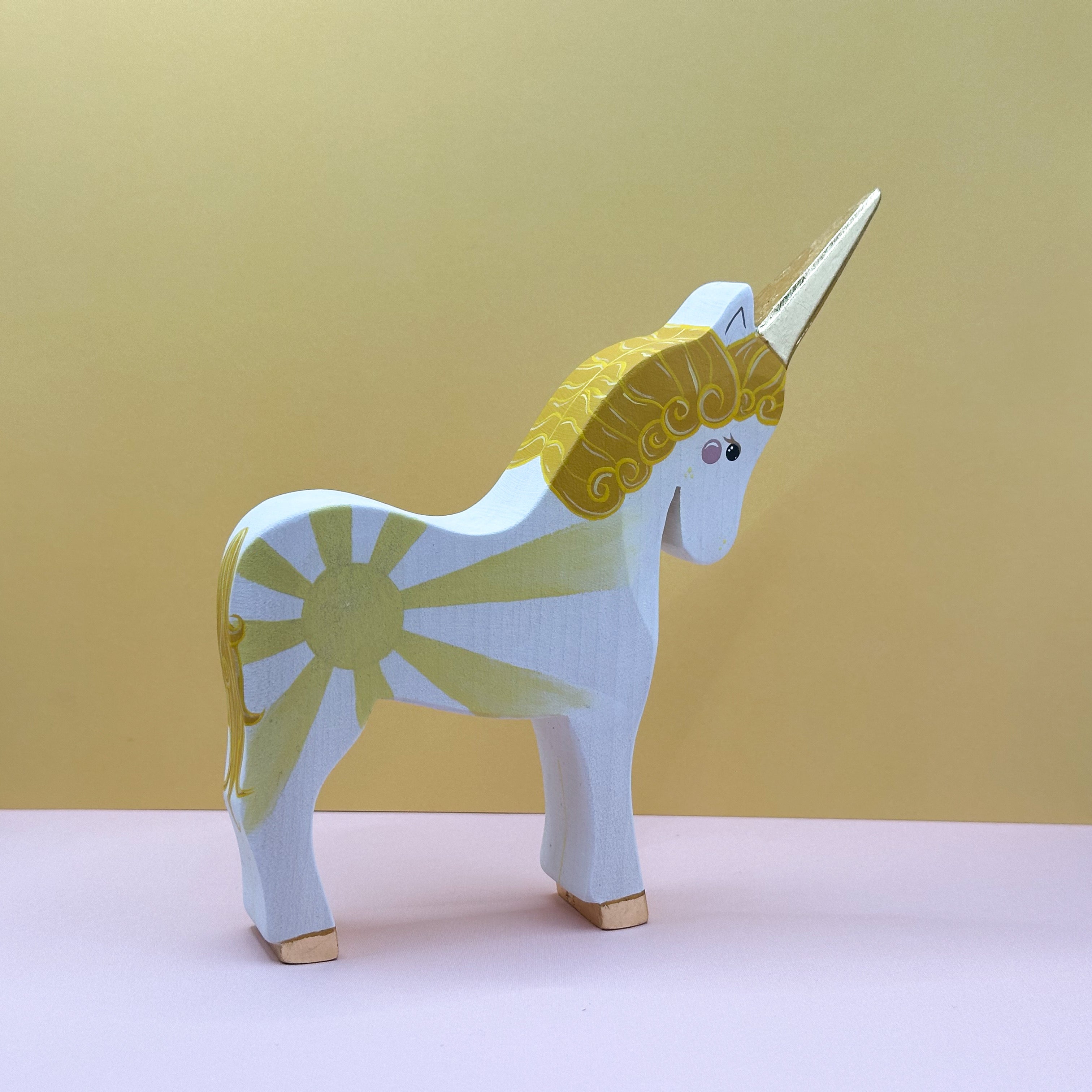 Wooden unicorn figurine with a yellow mane on a pink surface and yellow background