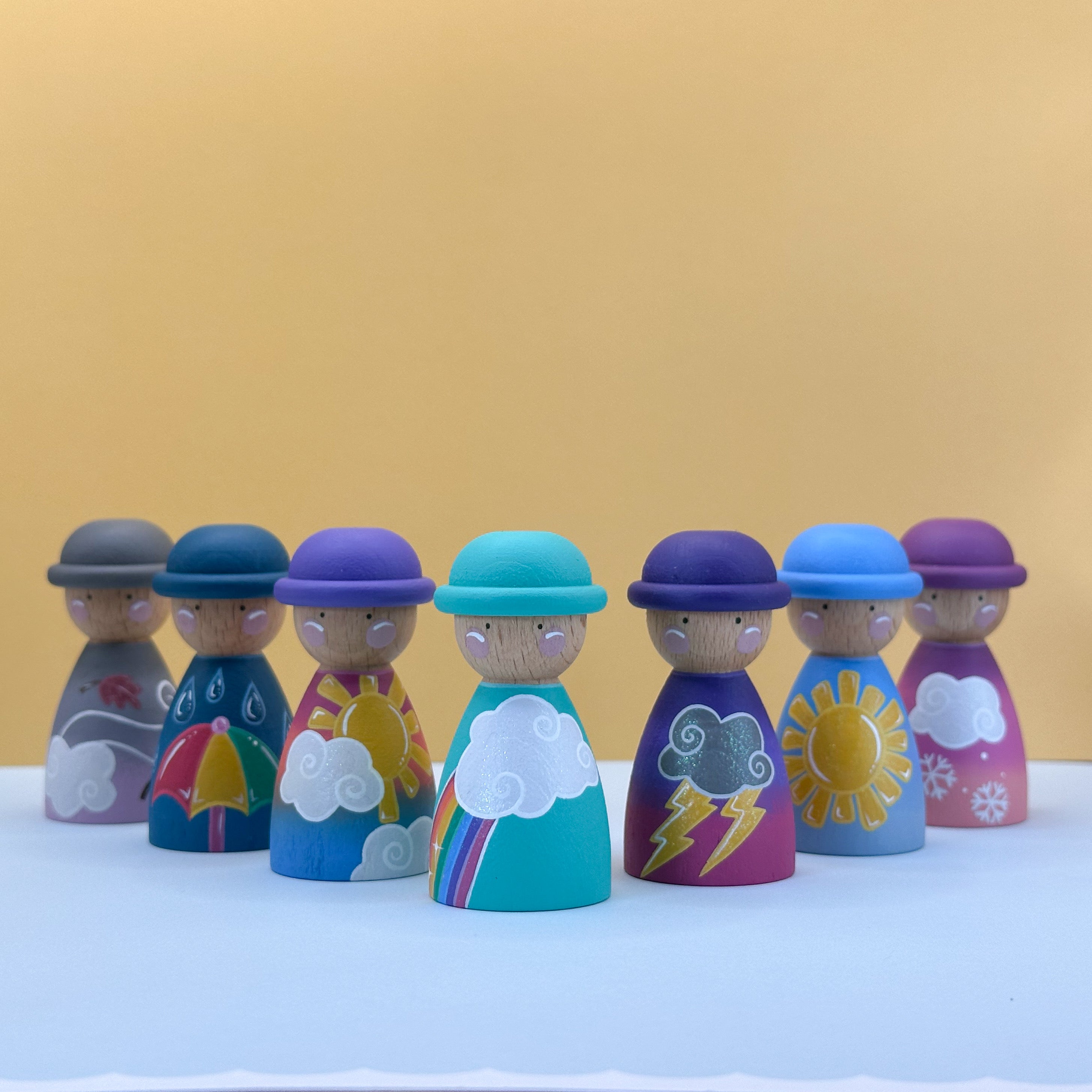 Set of colorful peg dolls with weather-themed designs on a white surface and yellow background