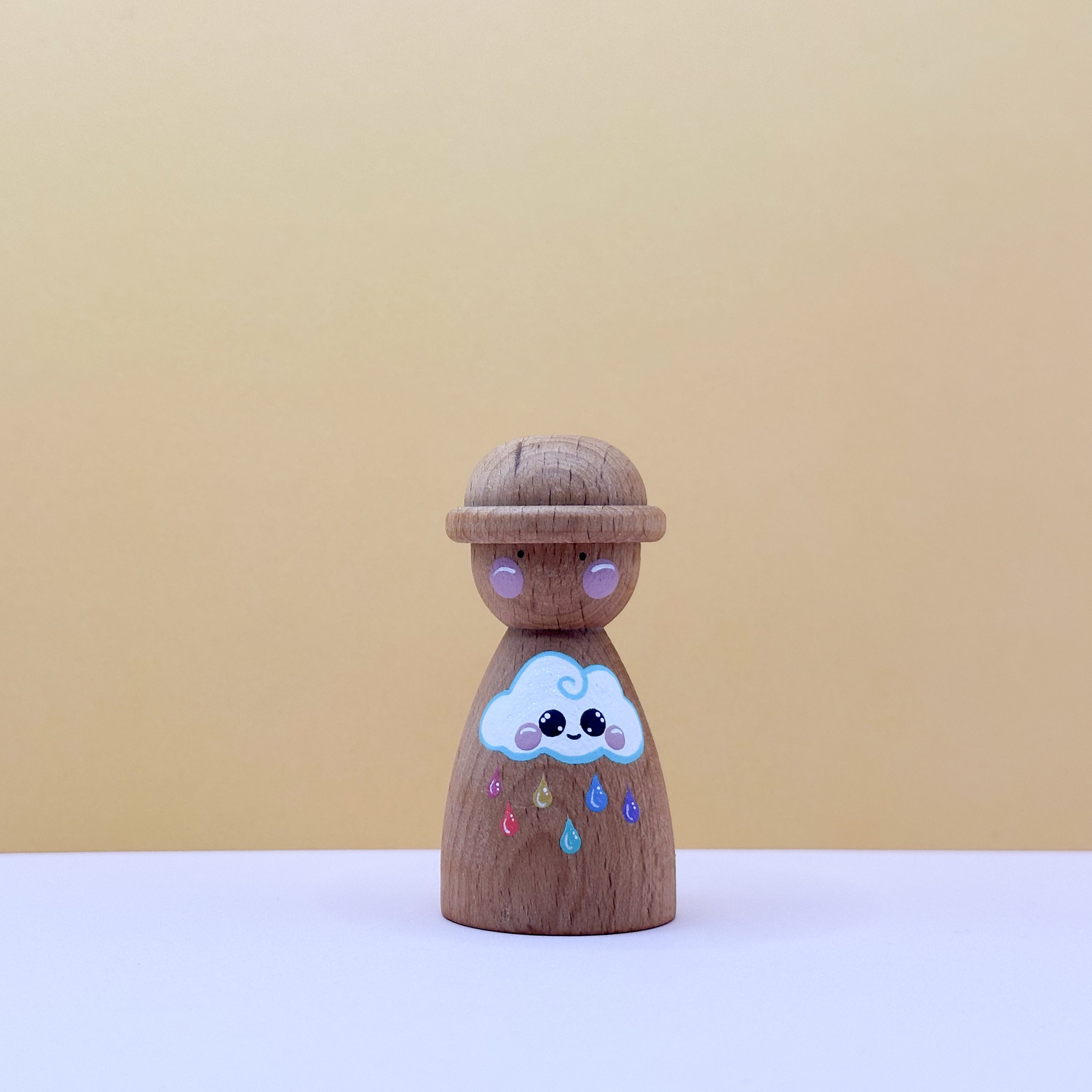Wooden peg doll with a cloud design on a beige background