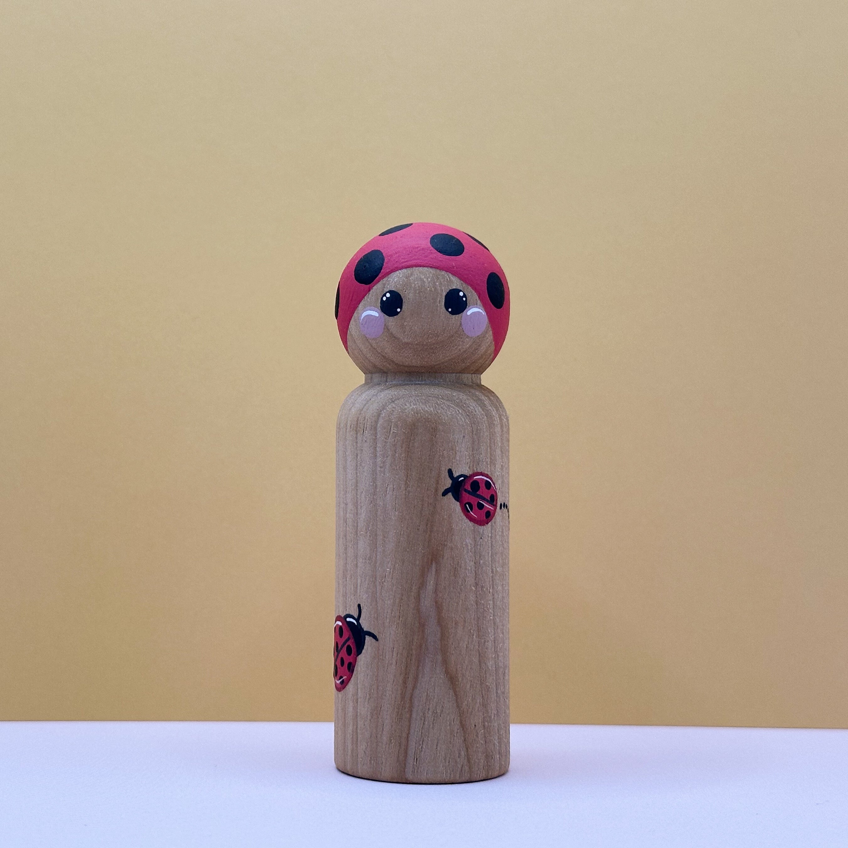 Wooden peg doll with a ladybug design on a beige background