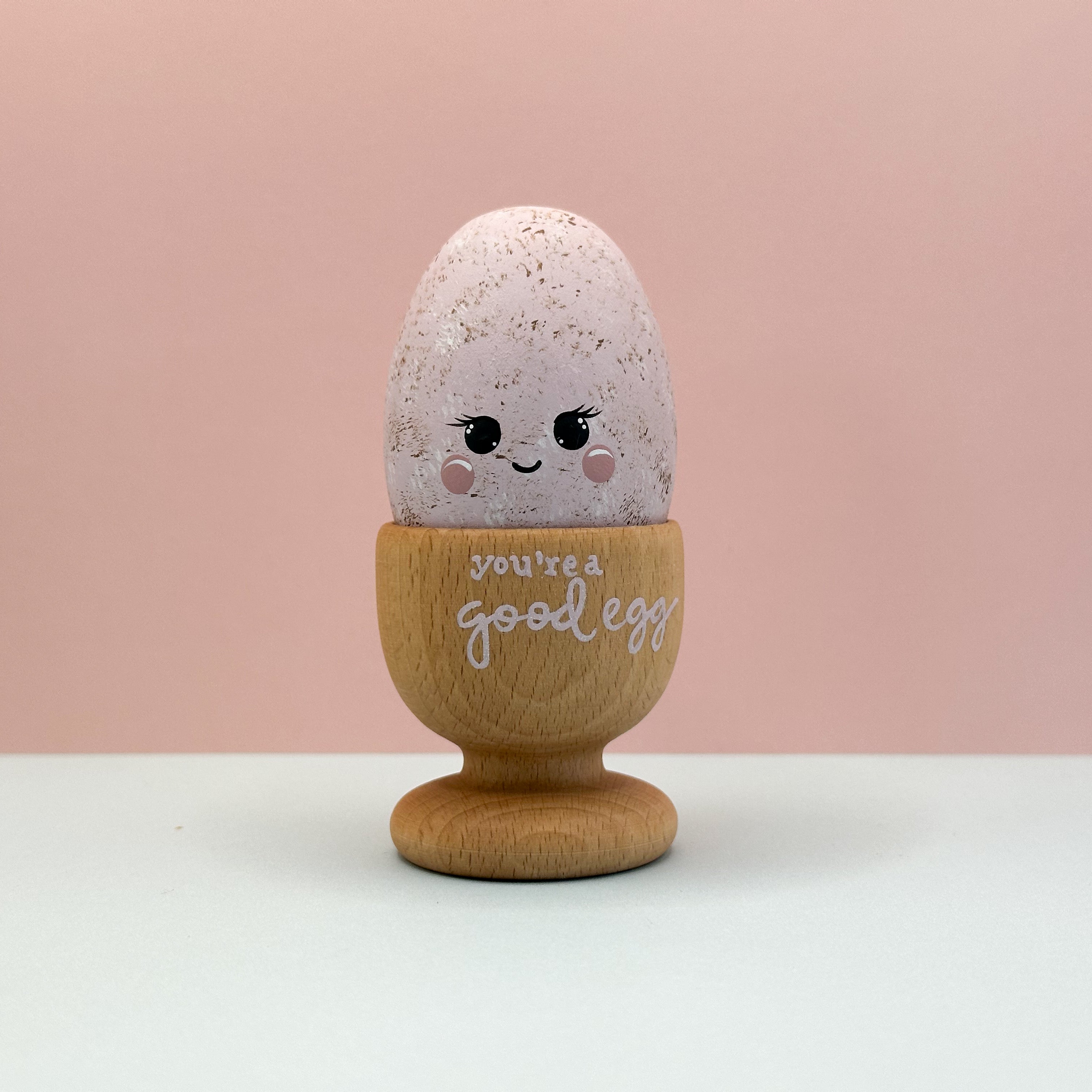 Decorative egg with a wooden stand and 'You're a good egg' text on a pink background