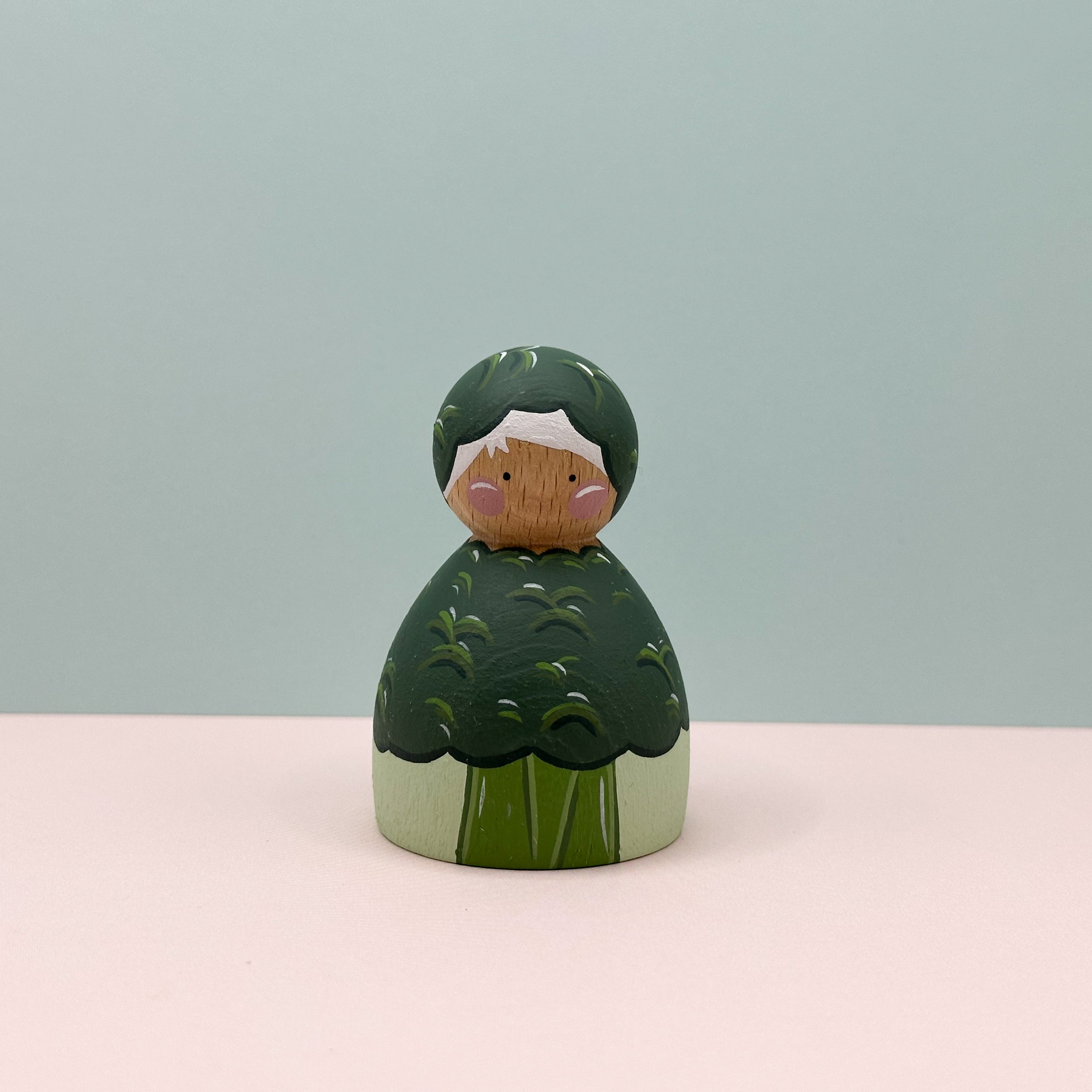 Wooden figurine with green broccoli dress and white face on a light gray background