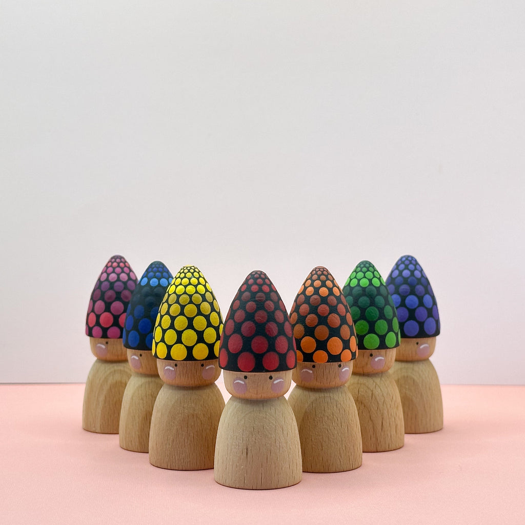 Wooden peg dolls with colorful headbands on a pink surface and light gray background