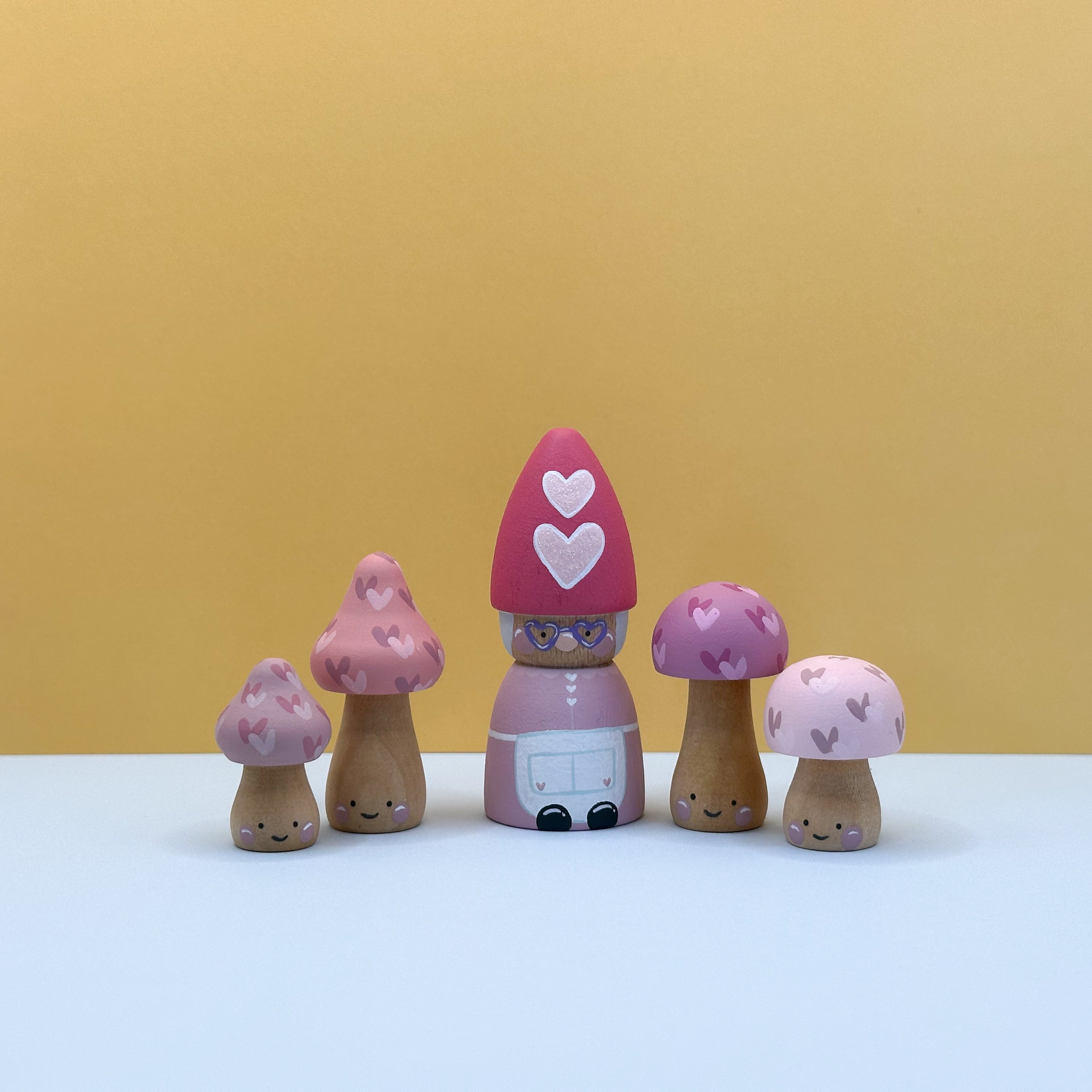 Set of wooden mushroom-shaped figurines with a pink top and heart design on a yellow background.