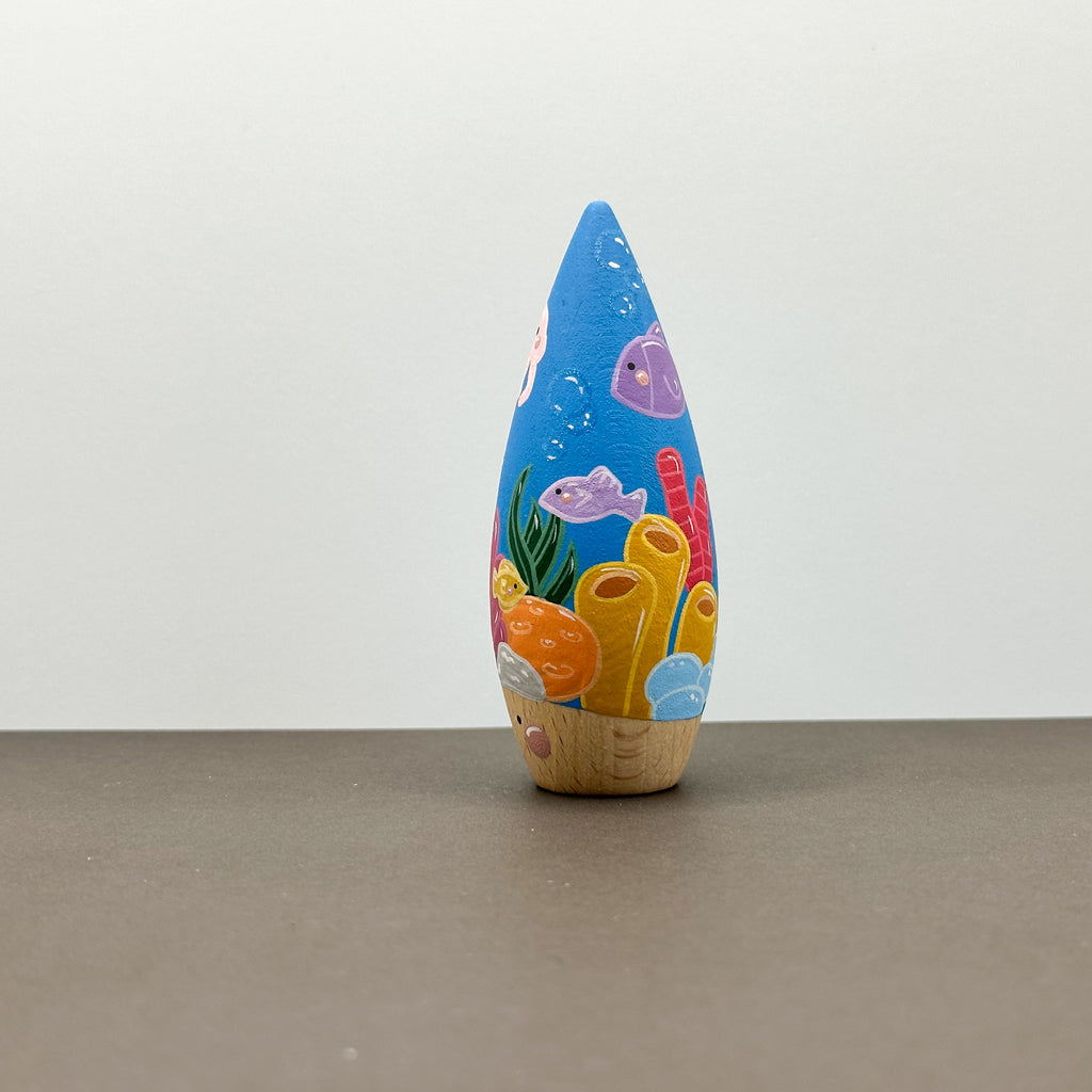 A wooden tear drop shaped toy with a coral reef theme on a grey background. 