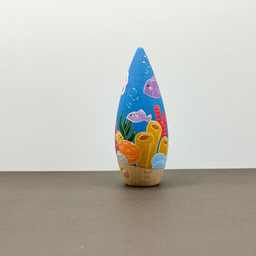 A wooden tear drop shaped toy with a coral reef theme on a grey background. 