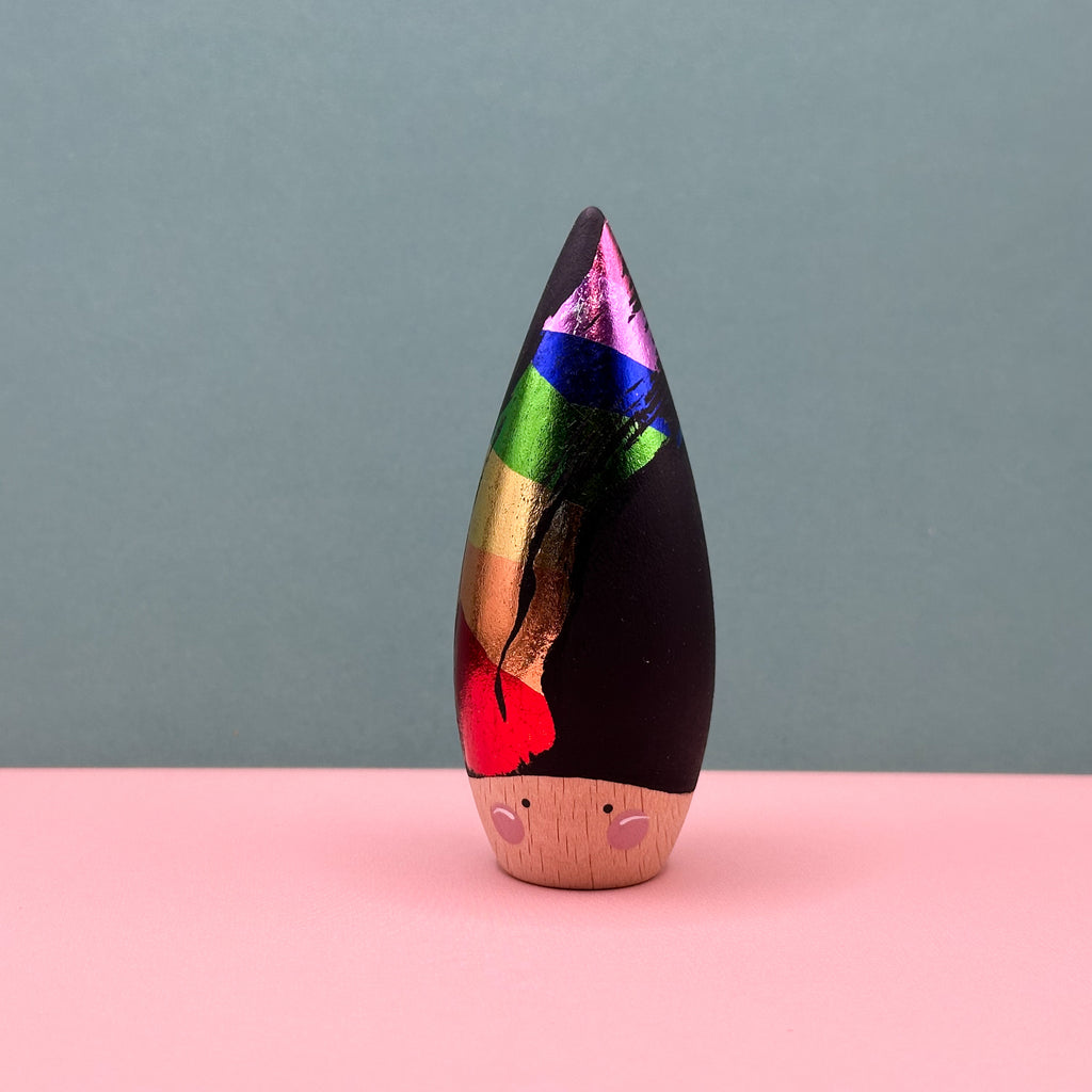 Wooden figurine with a colorful top and wooden base on a pink surface with a gray background