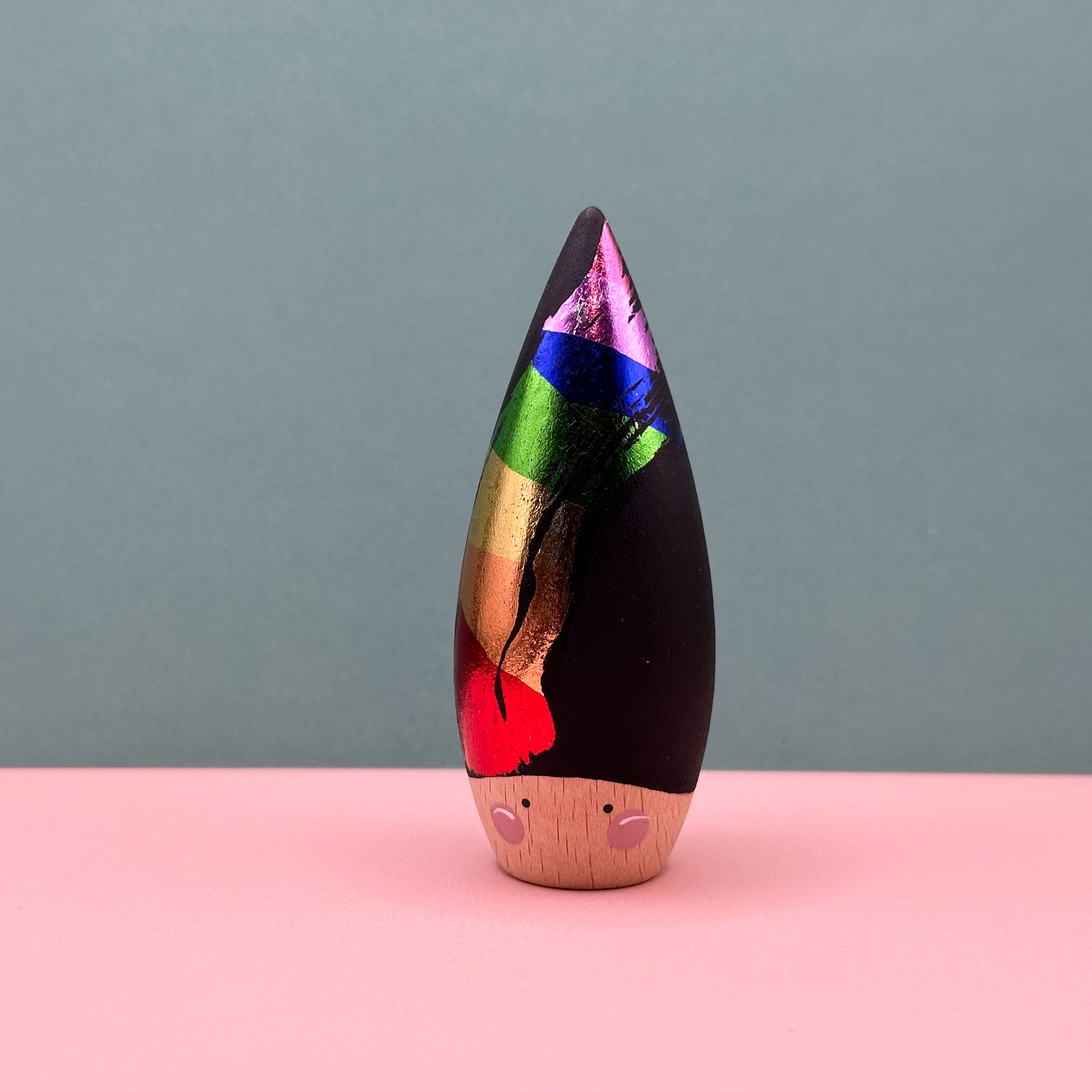 Wooden figurine with a colorful top and wooden base on a pink surface with a gray background