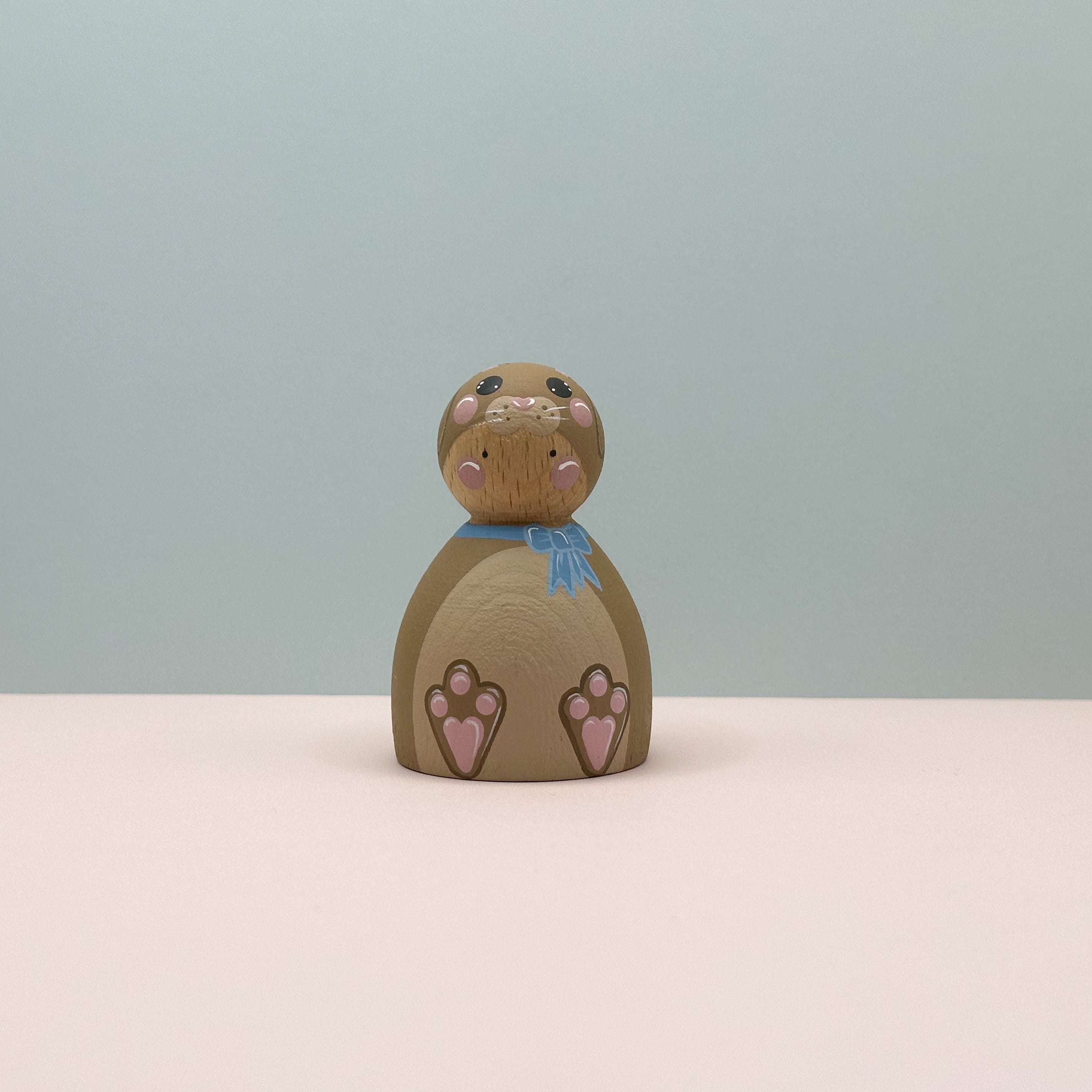 Wooden bunny figurine with pink paws on a light blue background