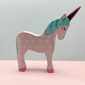 Pink unicorn figurine with a green mane and pink horn on a light pink surface with a light gray background