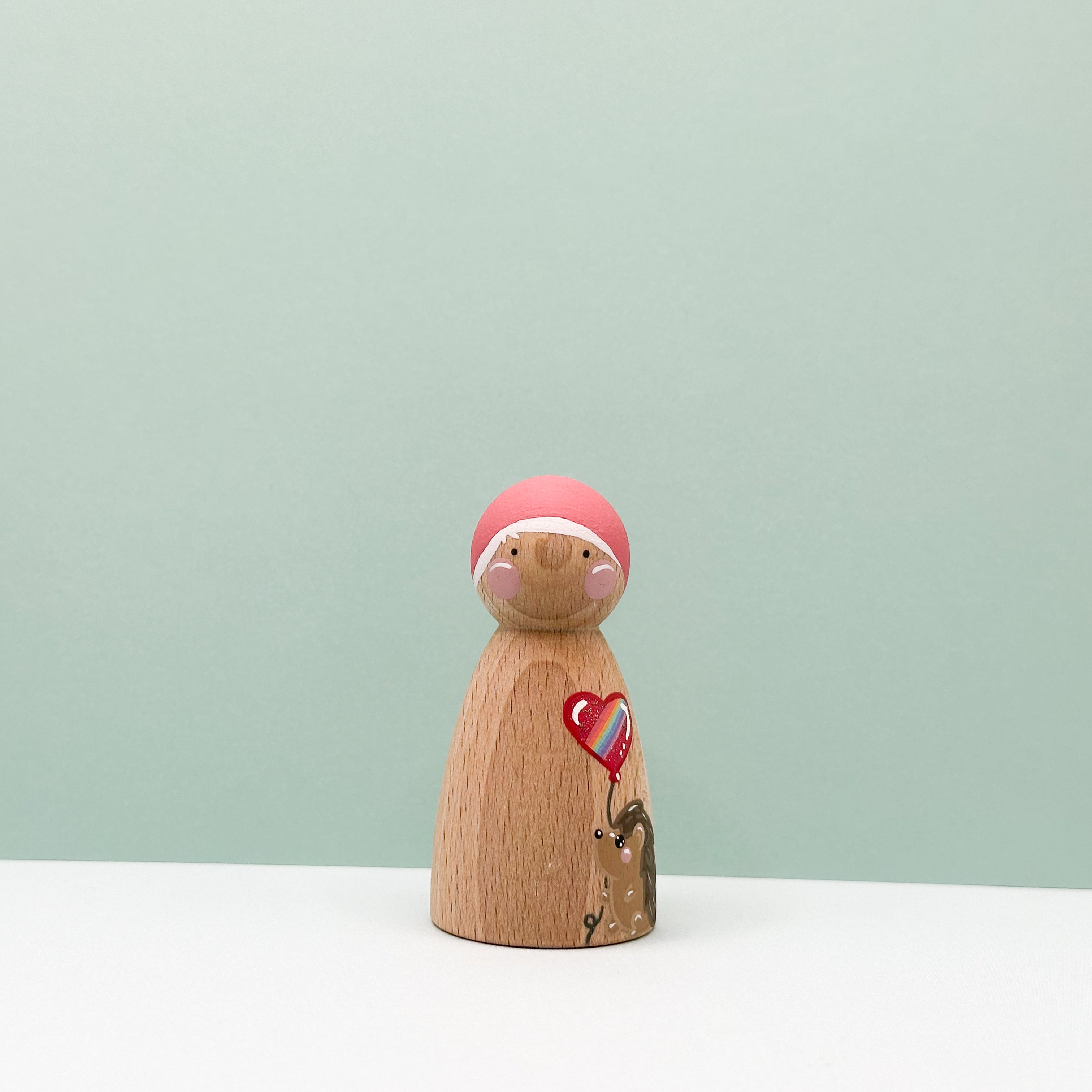 Wooden figurine with a pink hat and heart design on a light green background