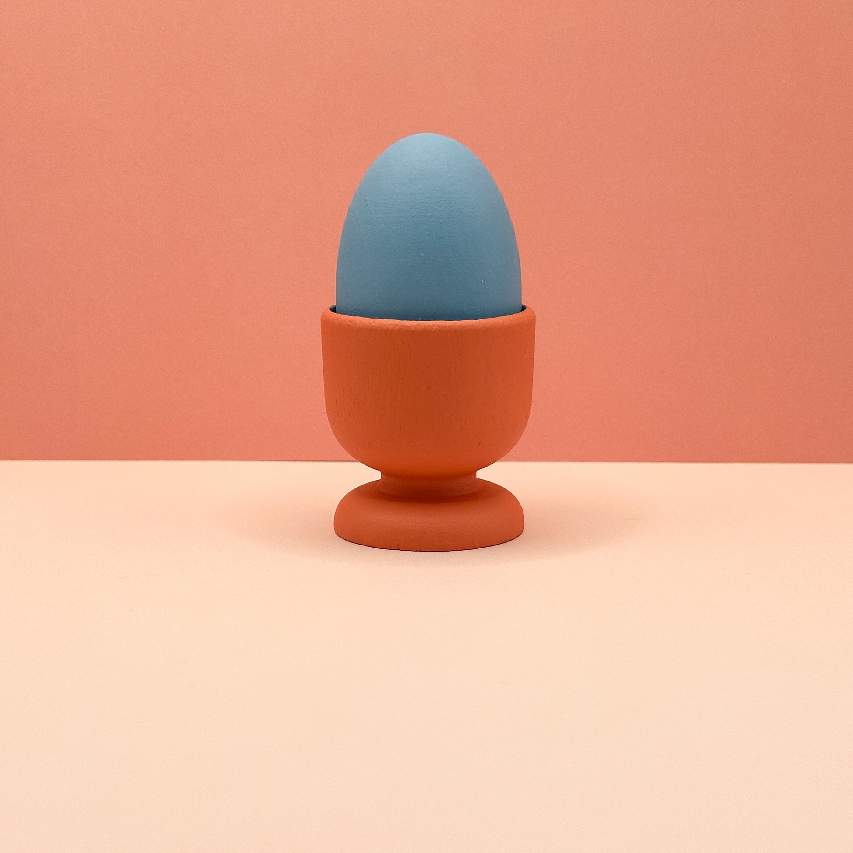 Blue egg in an orange holder on a peach background