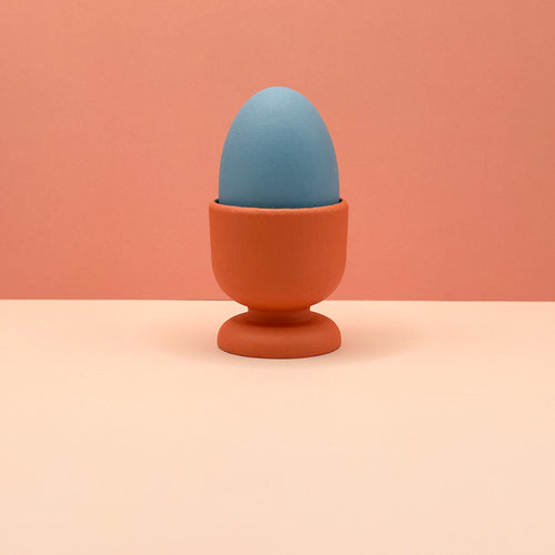 Blue egg in an orange holder on a peach background