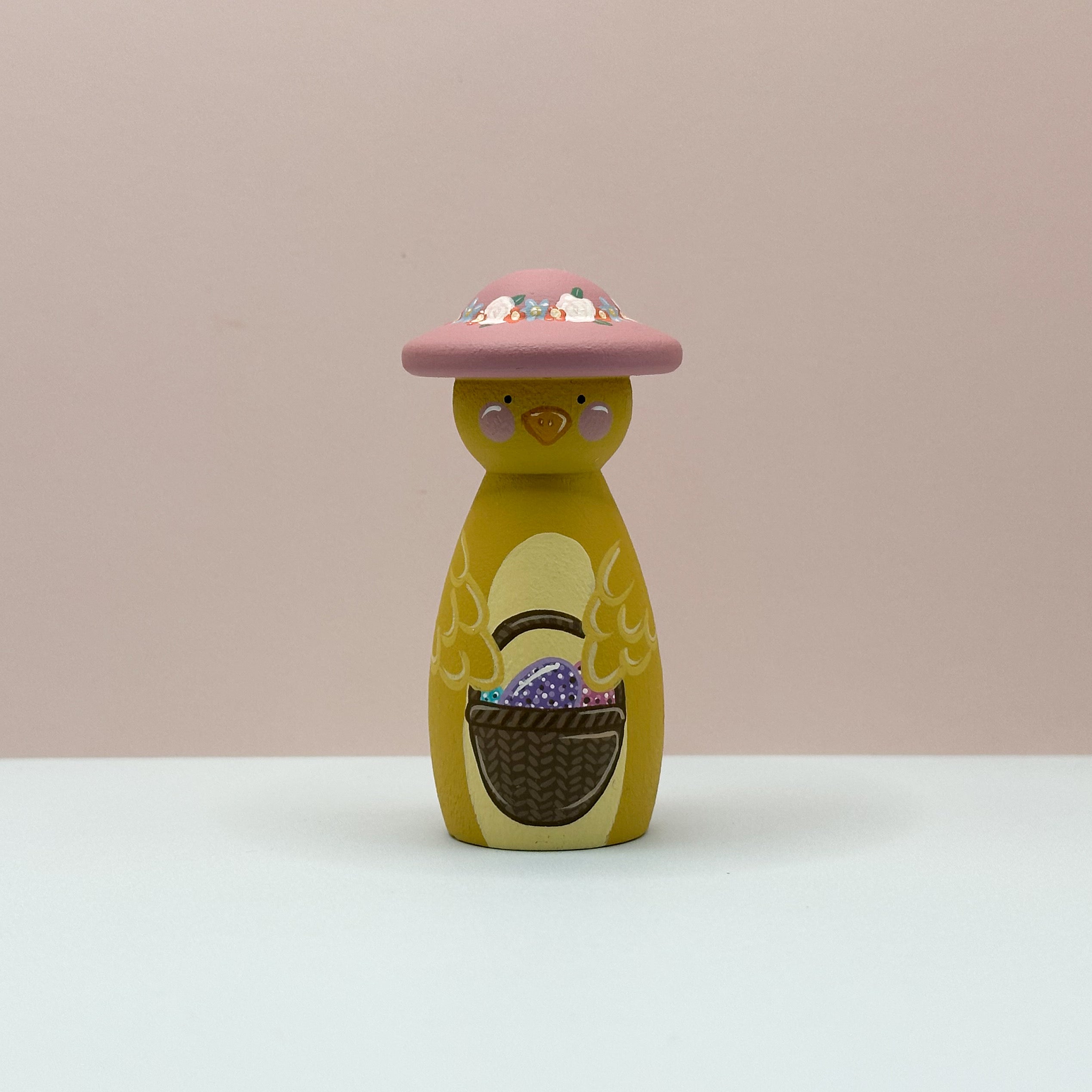 Yellow toy chick with a pink hat and Easter eggs on a beige background