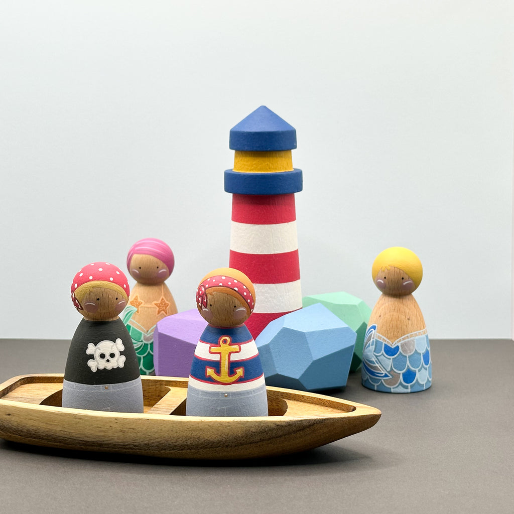 Pirate and mermaid themed peg doll toys with a wooden boat, wooden rocks and a lighthouse. 