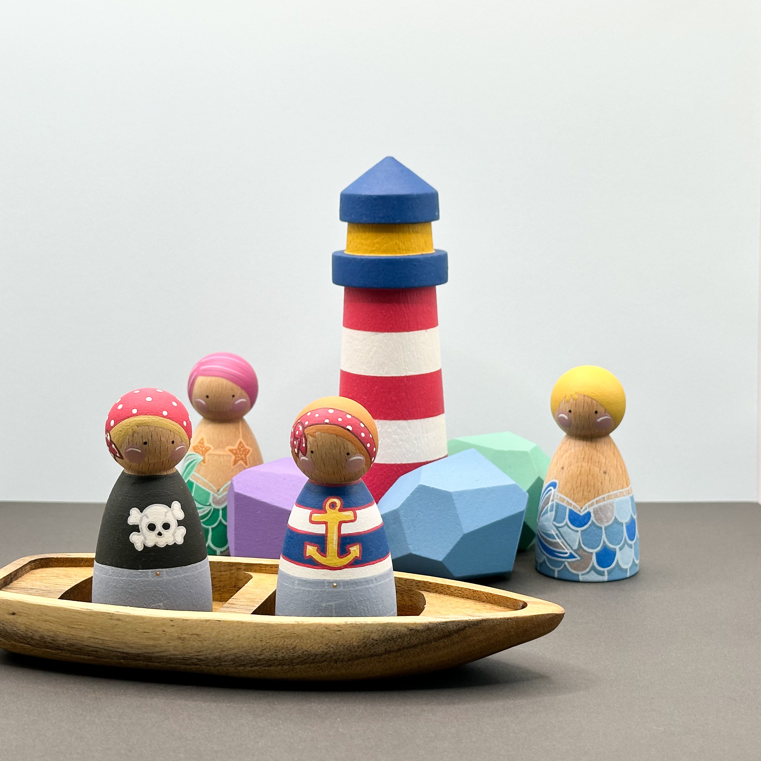Pirate and mermaid themed peg doll toys with a wooden boat, wooden rocks and a lighthouse. 