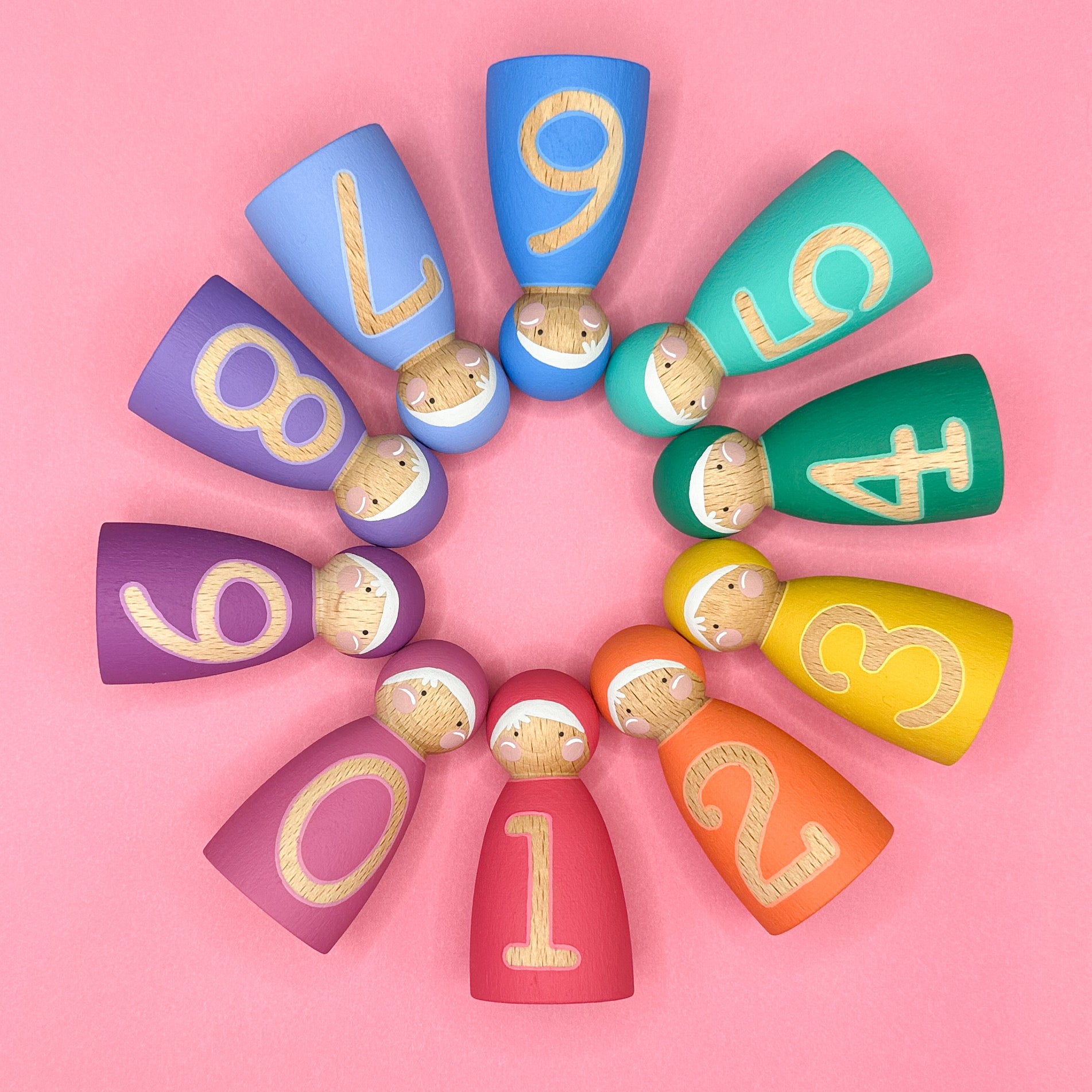 Colorful wooden dolls with numbers arranged in a circular pattern on a pink background