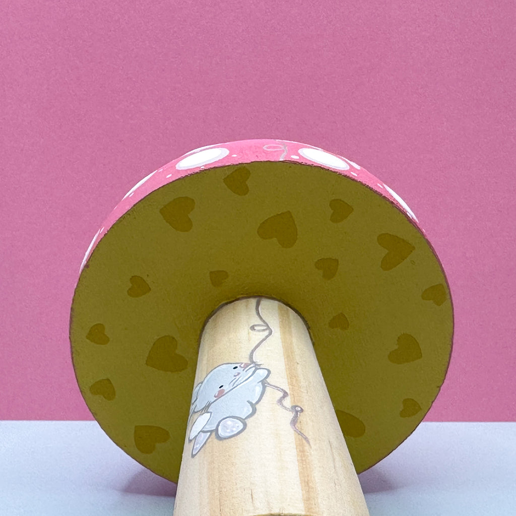 Wooden toy with a pink top and yellow underside featuring heart patterns on a pink background