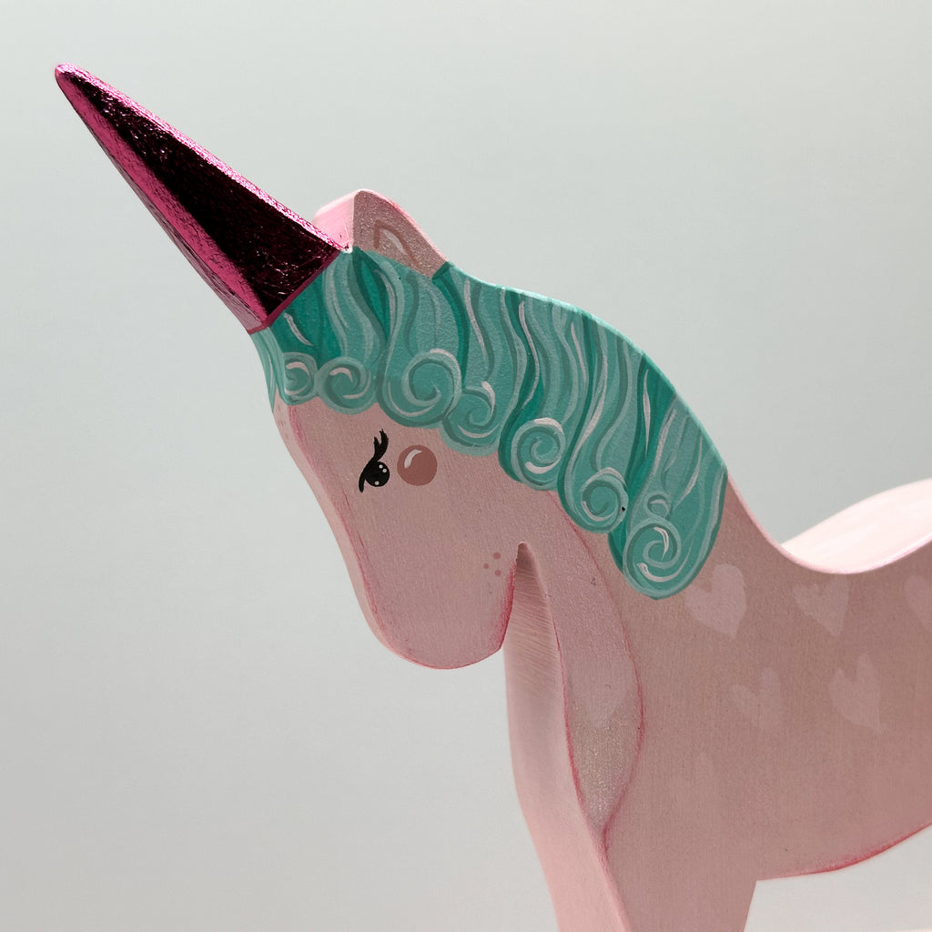 Pink unicorn figurine with teal mane and pink horn on a light gray background