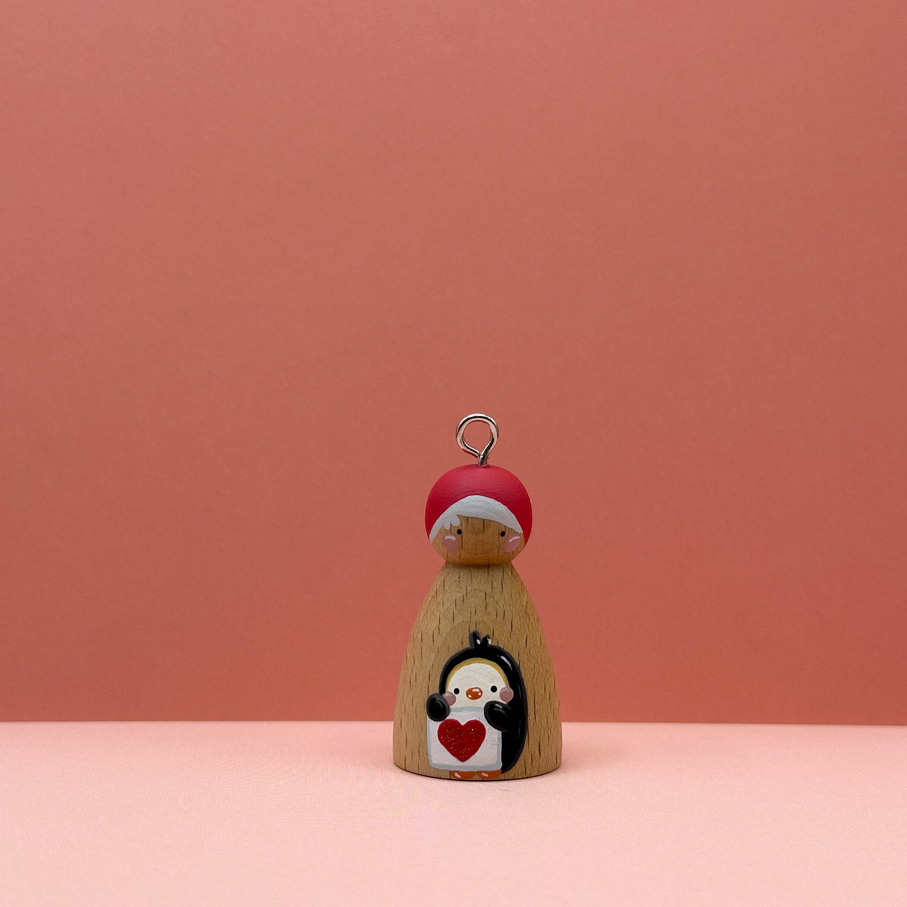 Small peg doll keyring with a Penguin holding a heart sign painted on its body with a peach background