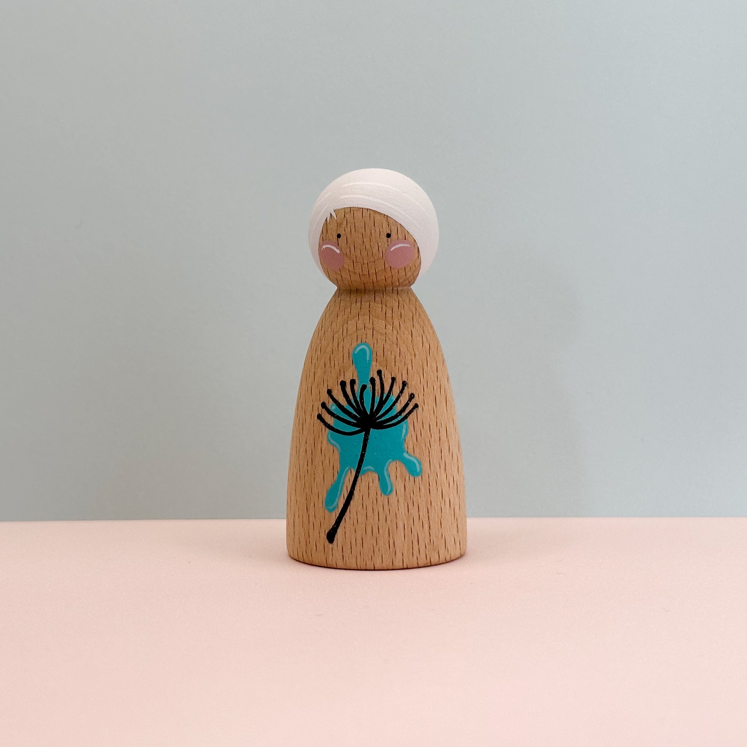 Wooden peg doll with a blue dandelion design on a light gray background