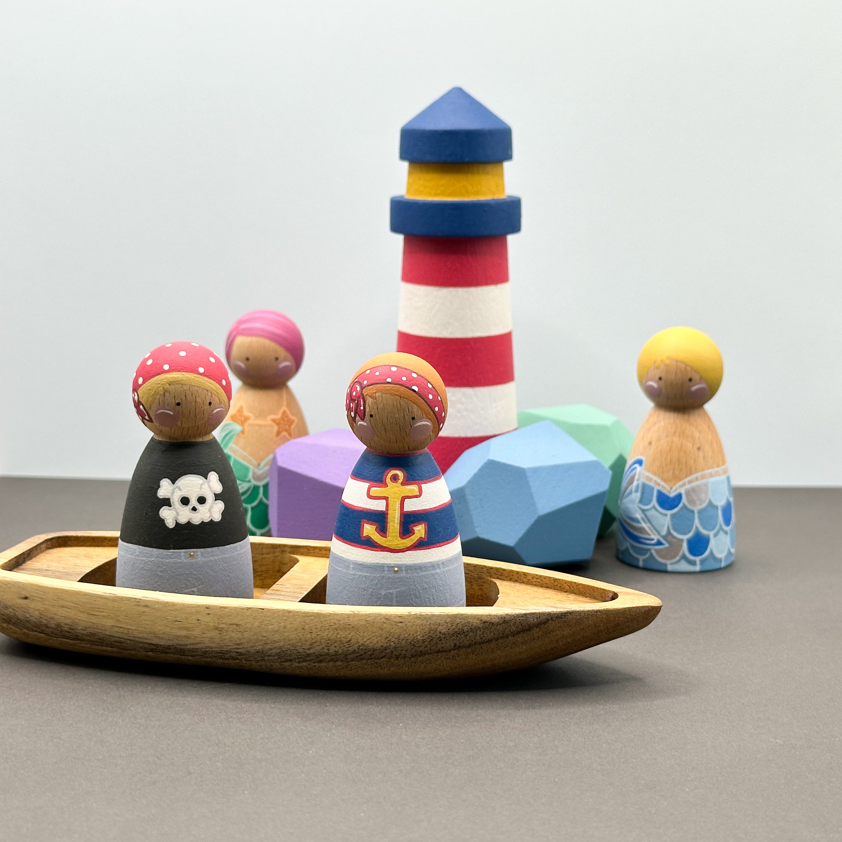 Pirate and mermaid themed peg doll toys with a wooden boat, wooden rocks and a lighthouse. 